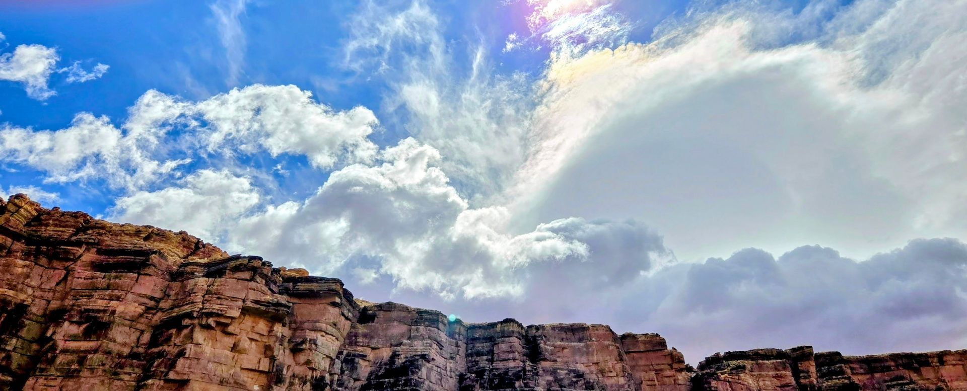 Dramatic sky with white clouds over a rocky canyon. Sun shines through the clouds.
