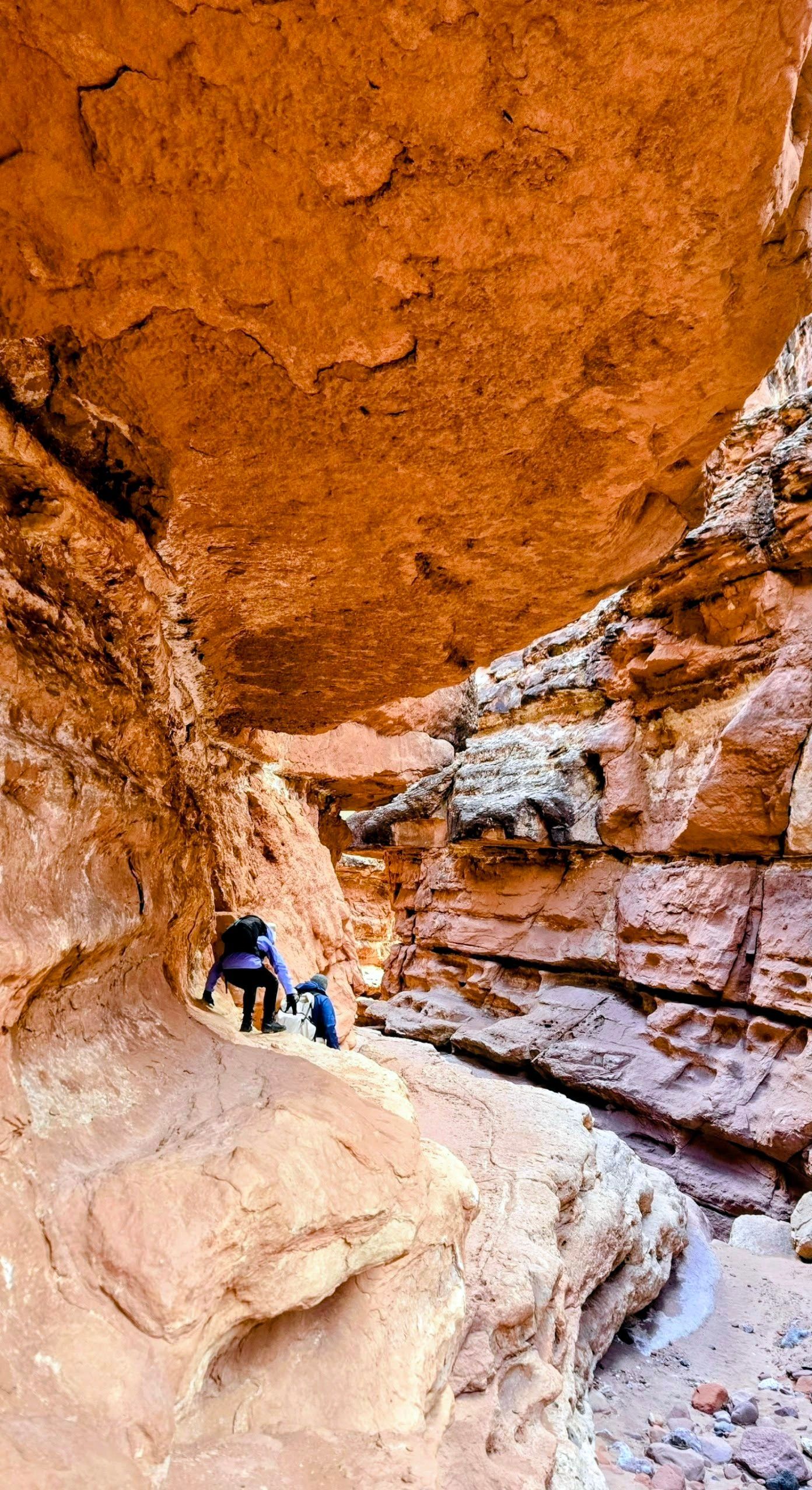 Hikers in a narrow red rock canyon. Sunlight illuminates the walls.