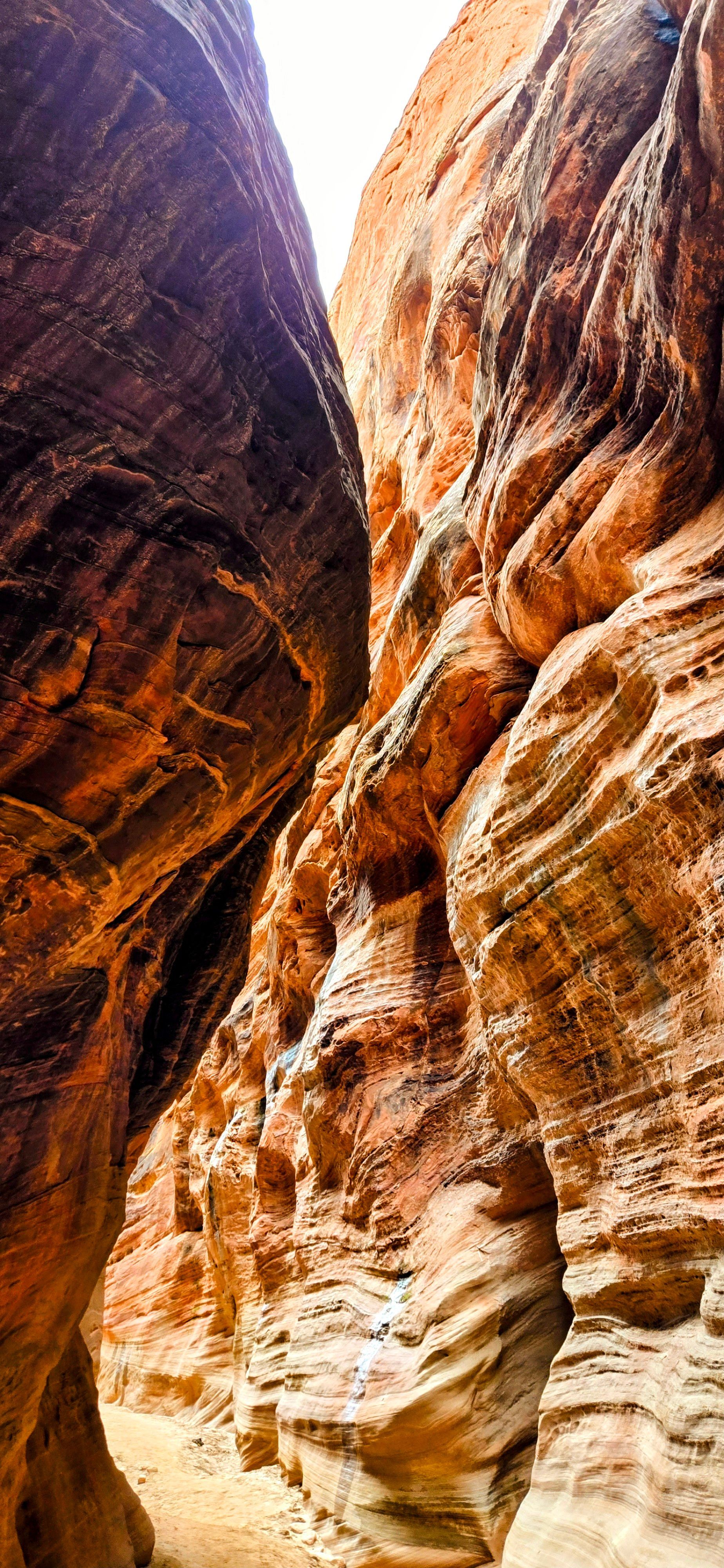 Narrow canyon with sandstone walls. Brown and orange rock formations. Sunlight at the top.