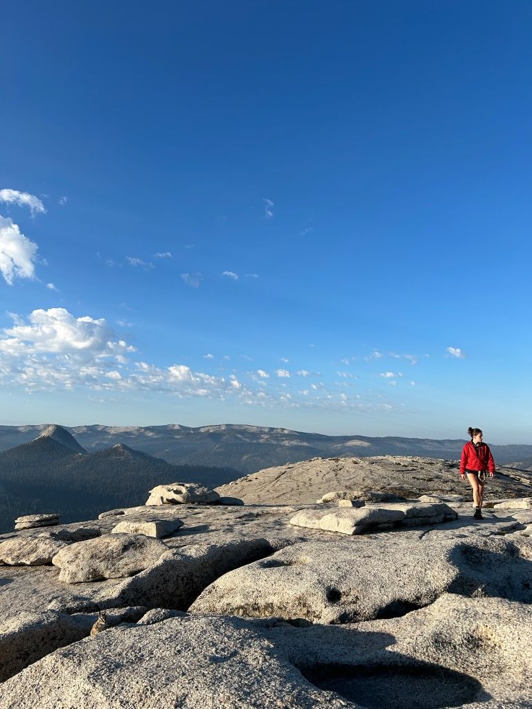 A person in a red jacket is standing on top of a rocky mountain.