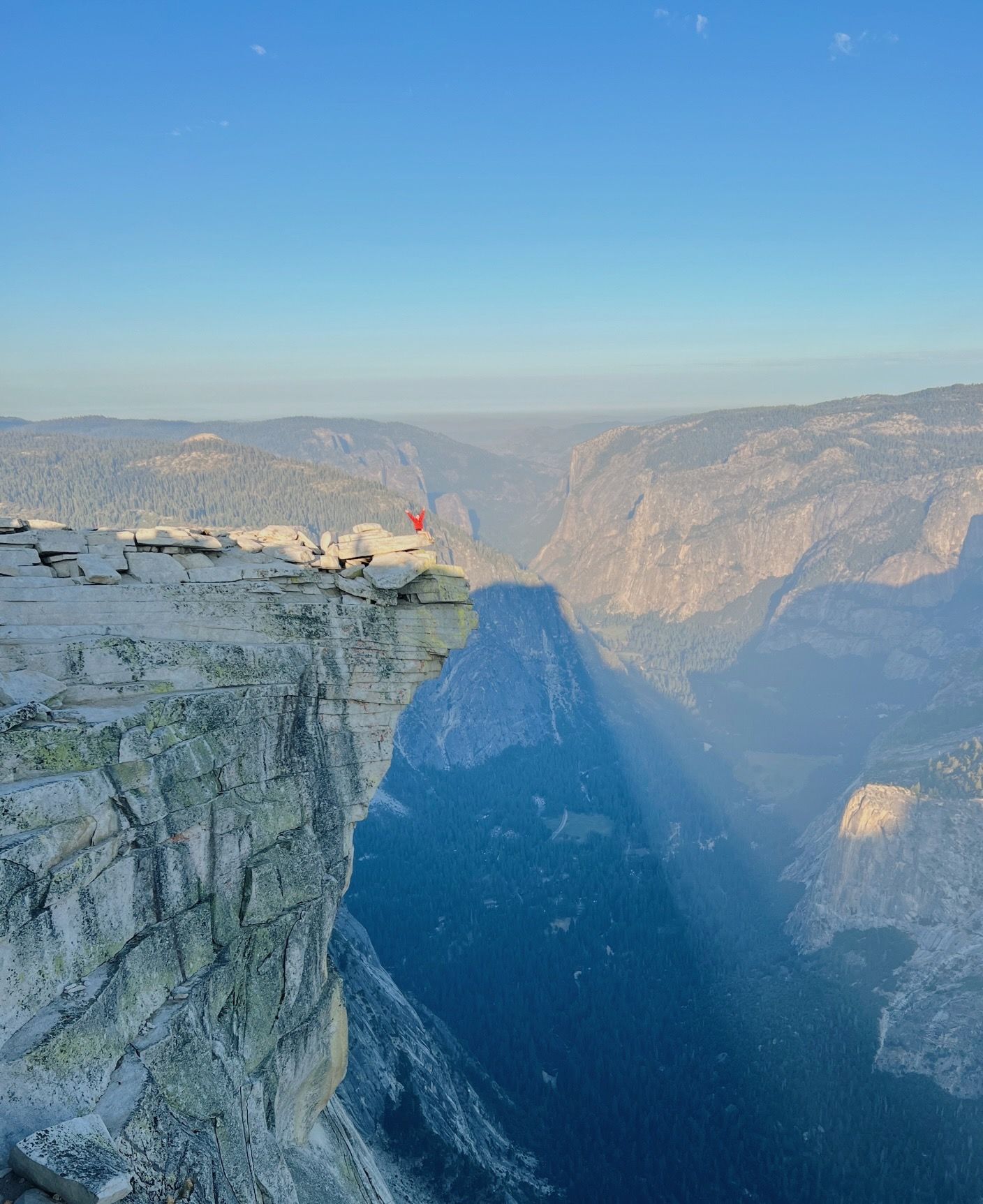 A person is standing on the edge of a cliff overlooking a valley.