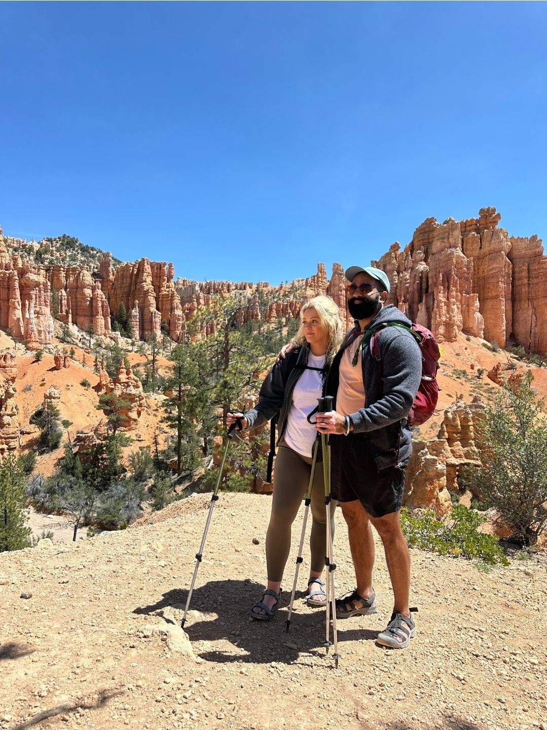 Two hikers pause on a trail in a canyon. They use trekking poles and backpacks. Sunny day.