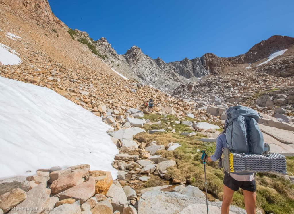 A woman with a backpack is hiking up a mountain.