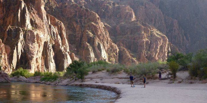 A couple of people are walking on a beach next to a river.