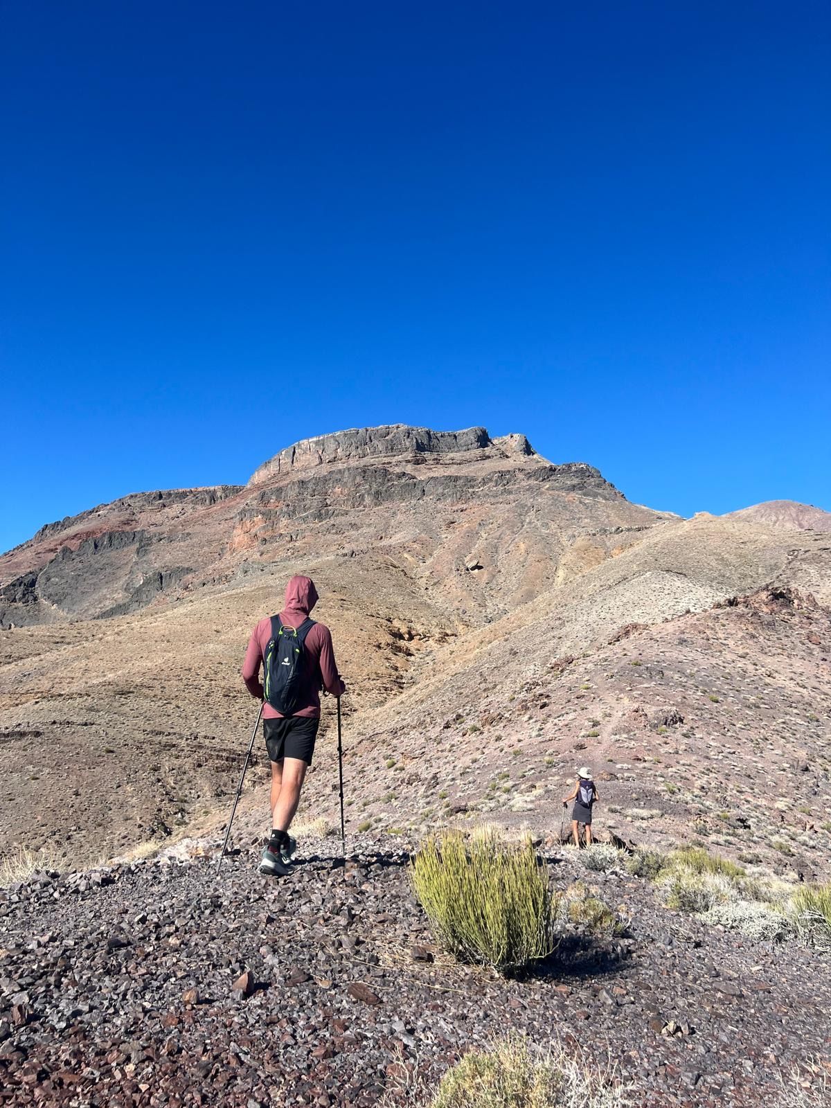 Hikers ascending a rocky mountain trail under a clear blue sky.