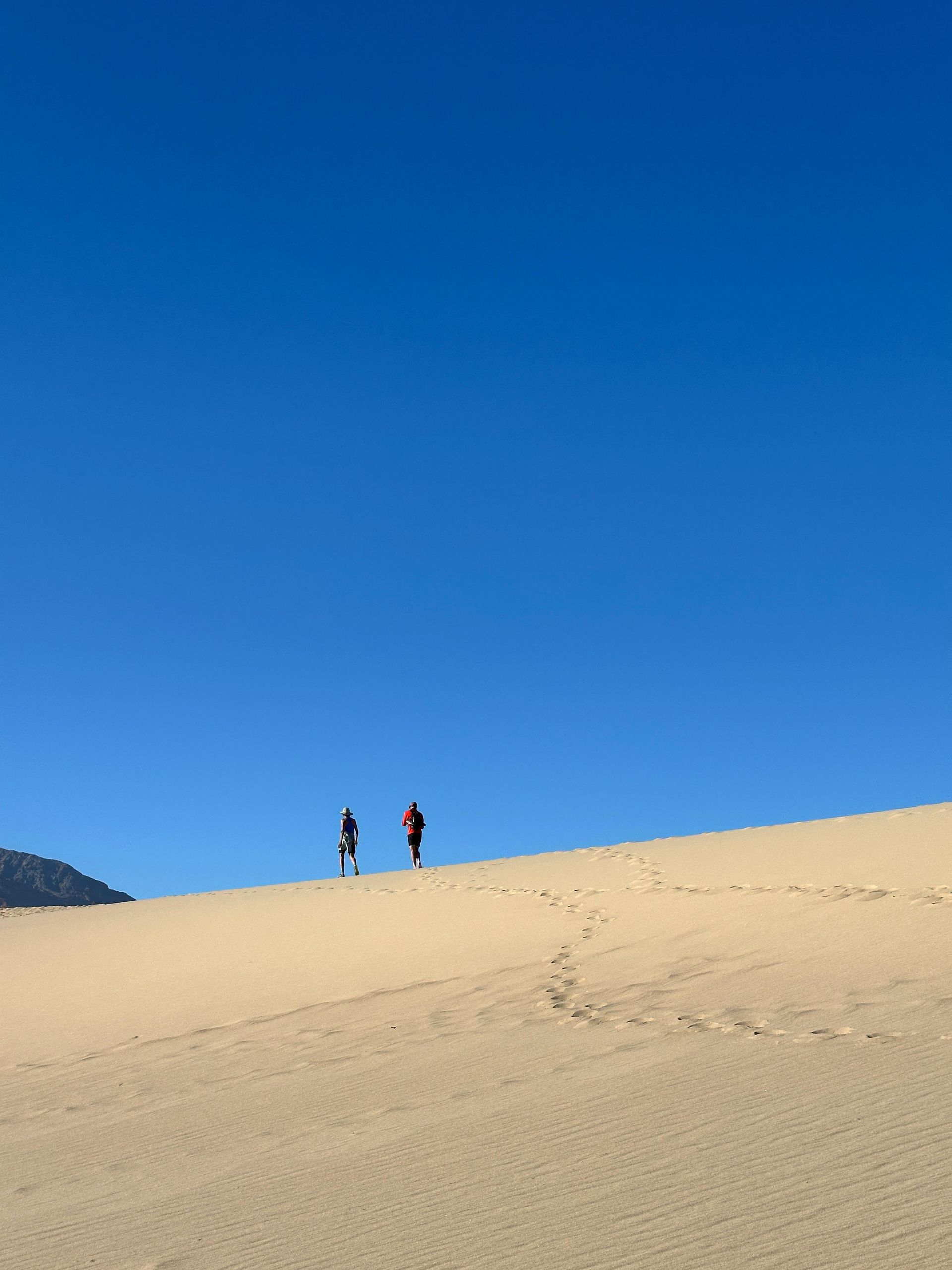 Two people walking on a sand dune under a clear blue sky.