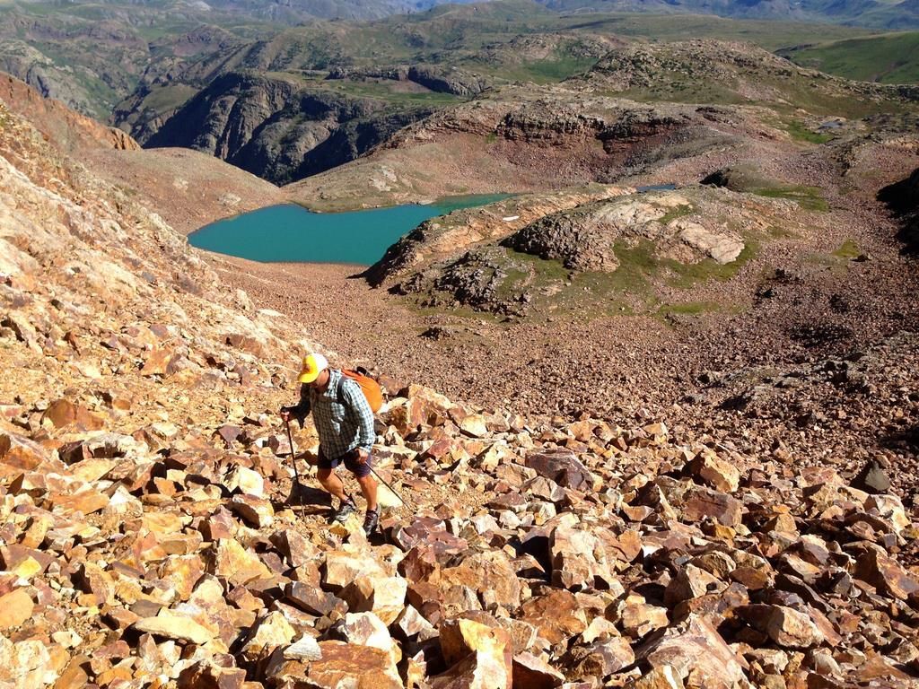 A person is walking up a rocky hill with a lake in the background.