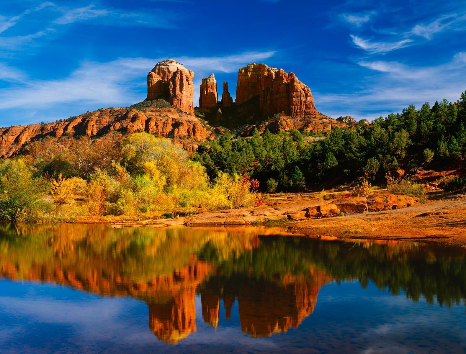 A large rock formation is reflected in a lake surrounded by trees.