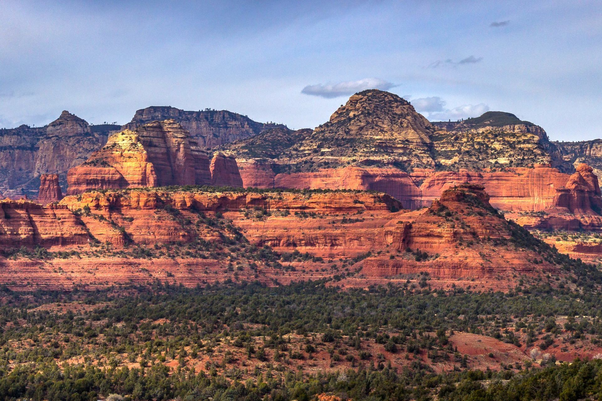 Sunlit red rock cliffs with layered mesas above a green desert foreground