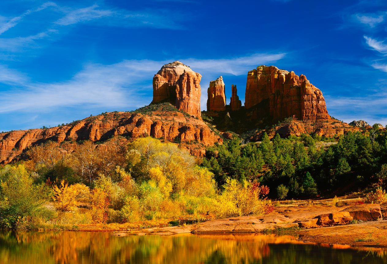 A large rock formation is reflected in a lake surrounded by trees.