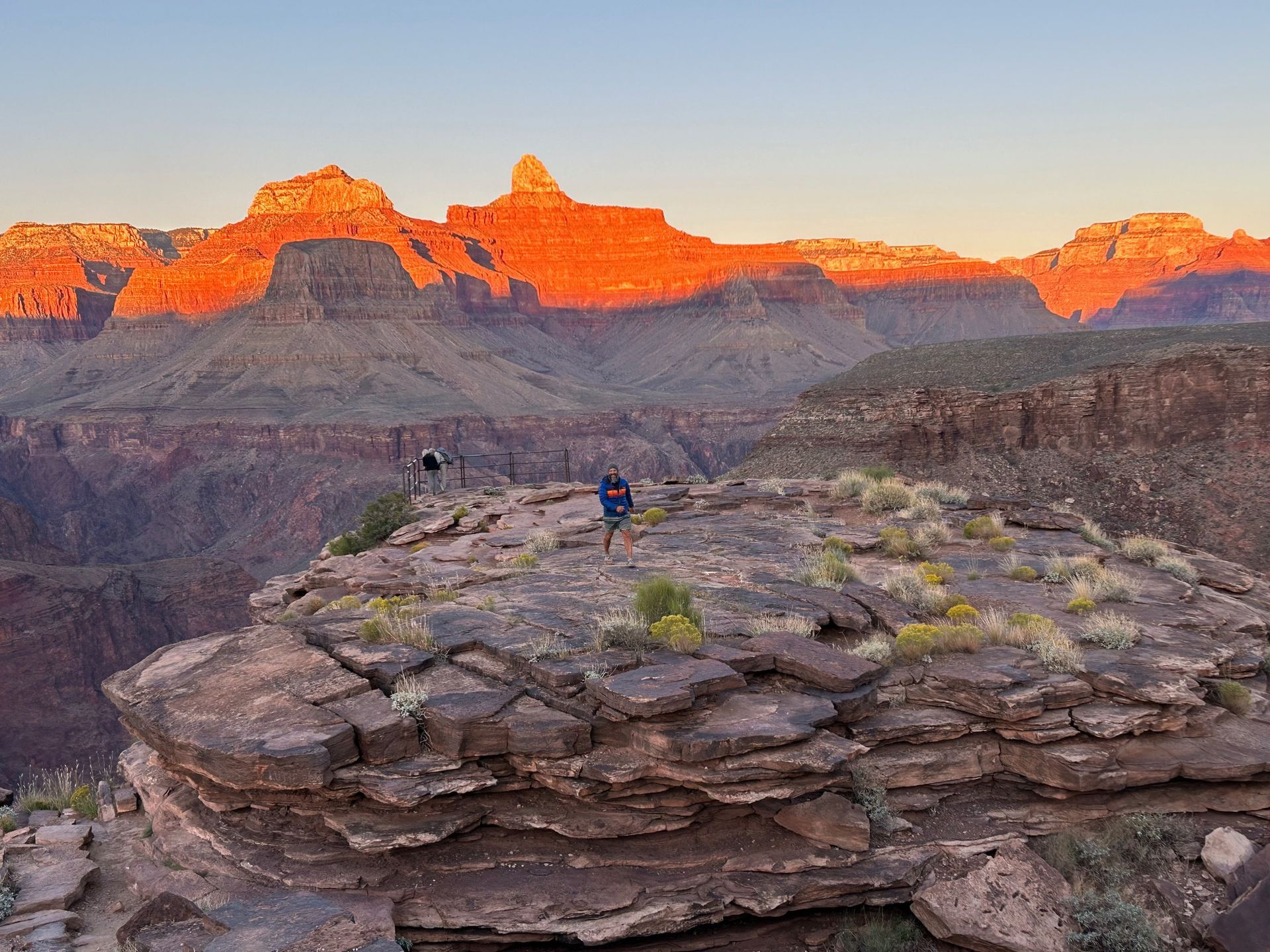A couple of people are standing on top of a rocky cliff overlooking a canyon.