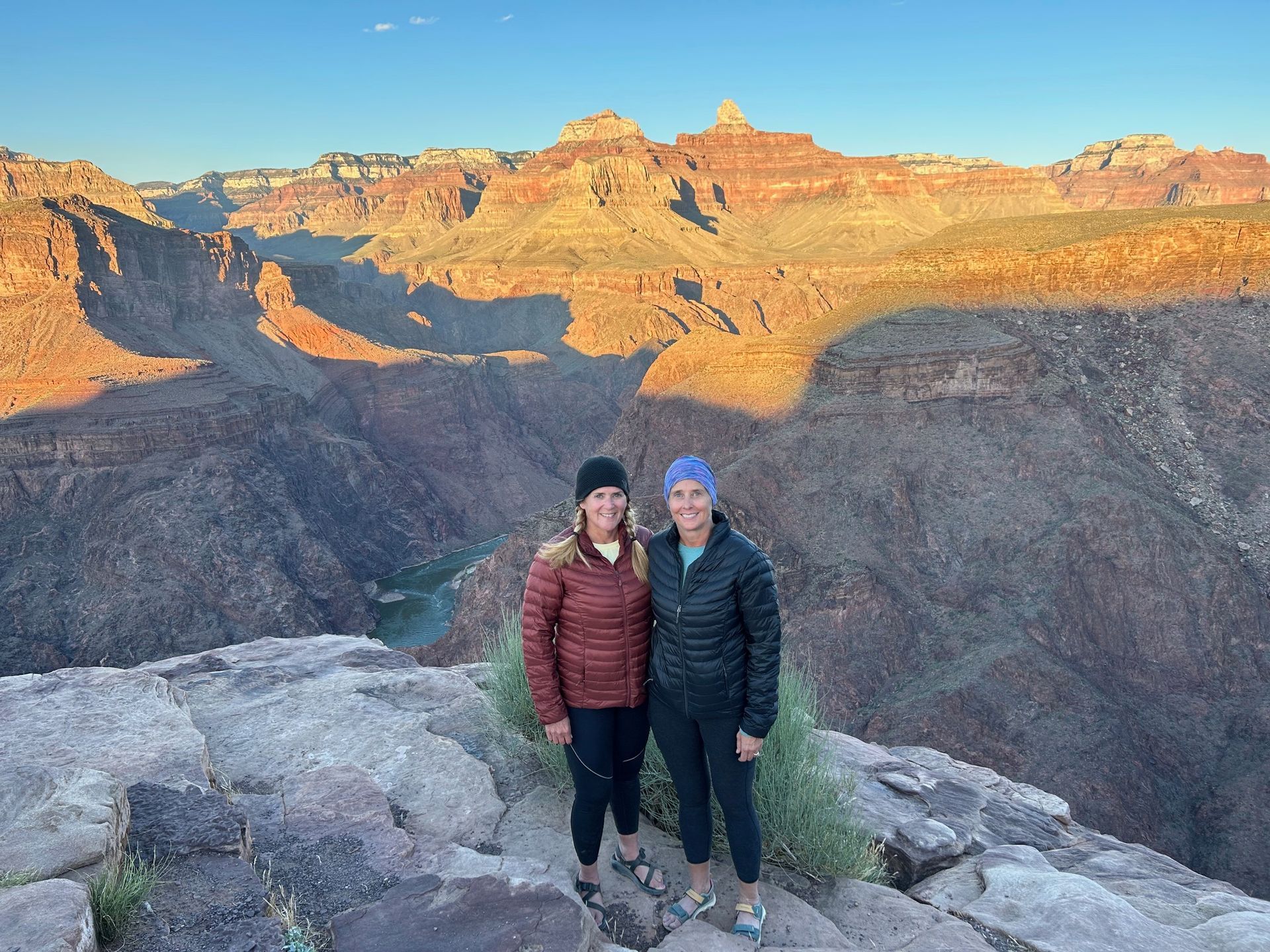 Two women are standing on top of a rocky cliff overlooking a canyon.