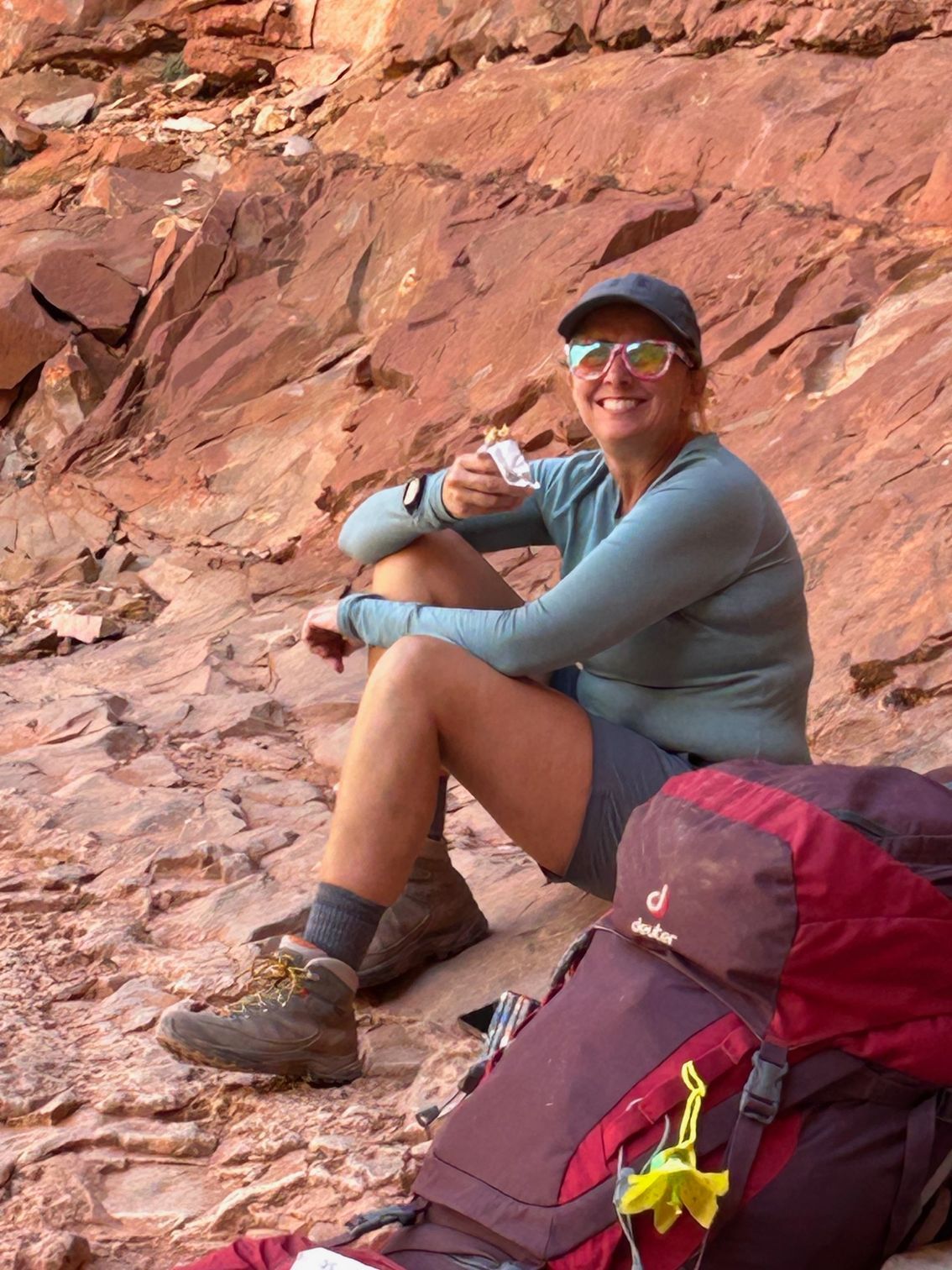 A woman is sitting on a rock next to a backpack.