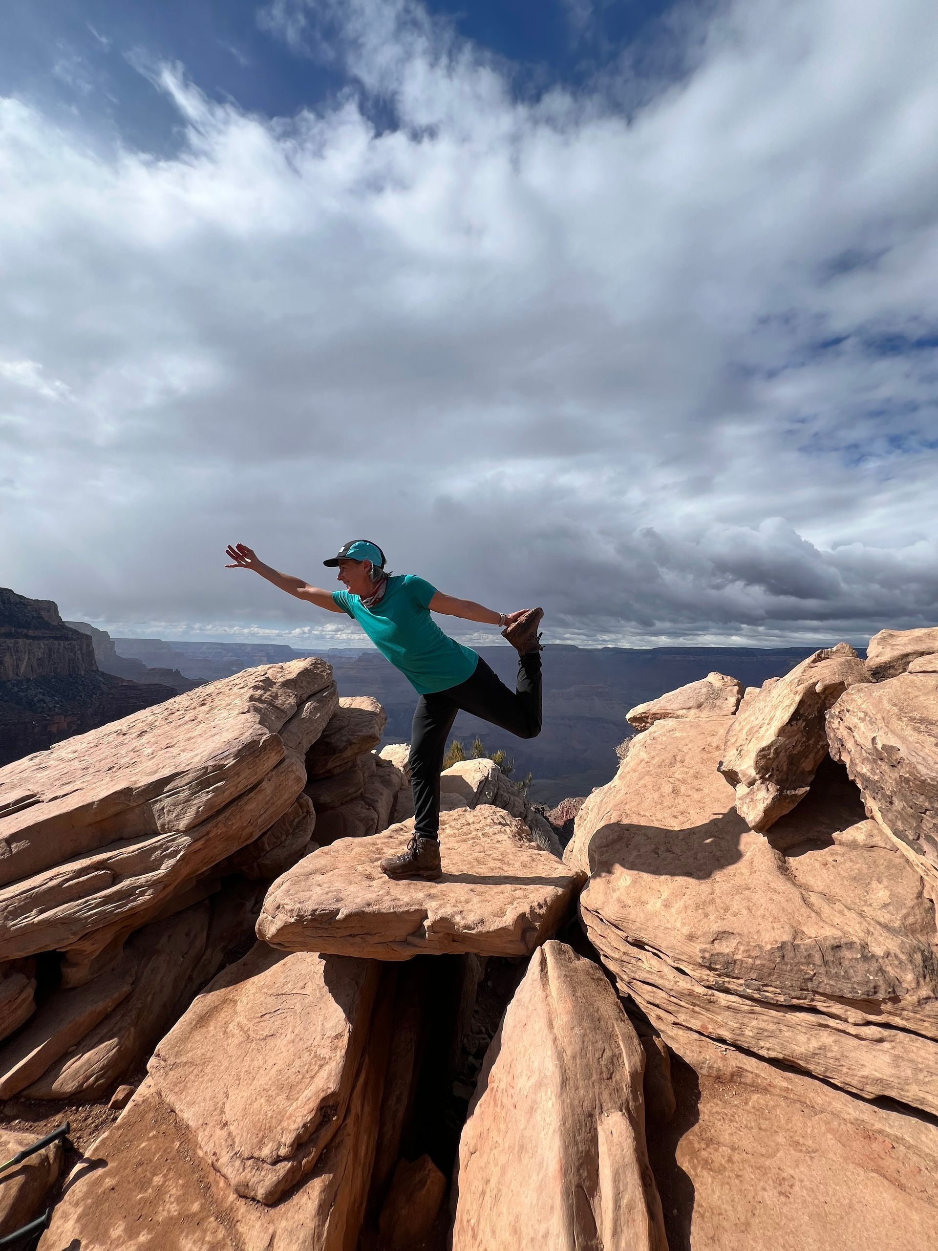 A woman is standing on one leg on top of a rocky cliff.