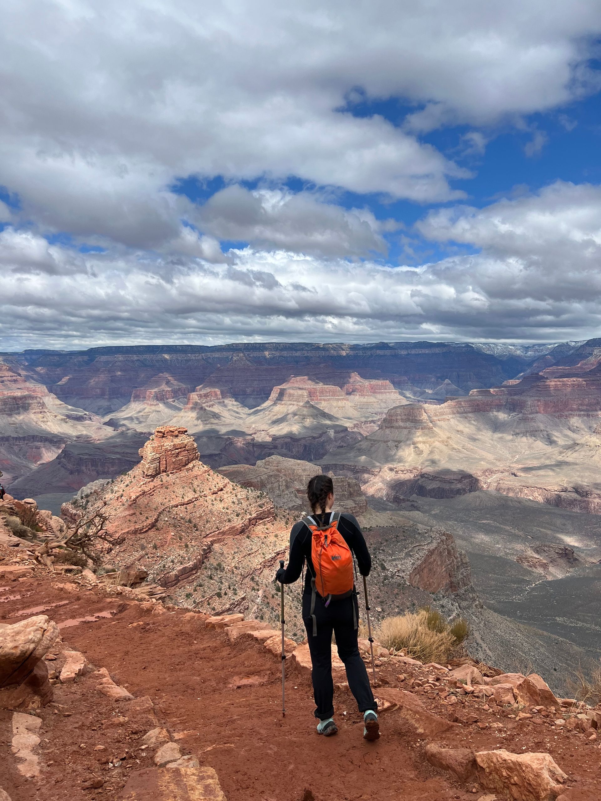 A person with an orange backpack is standing on top of a mountain.