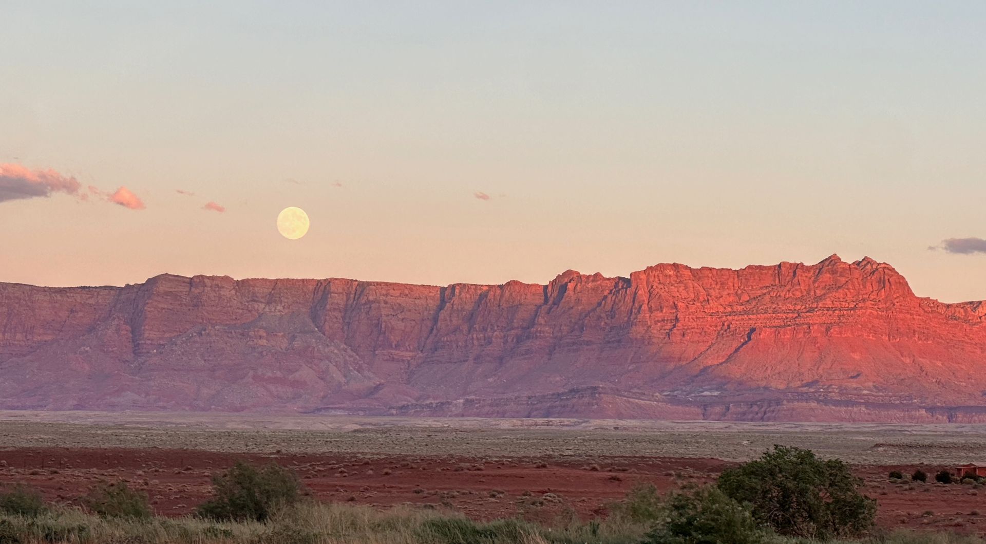 A full moon is rising over a mountain range in the desert.