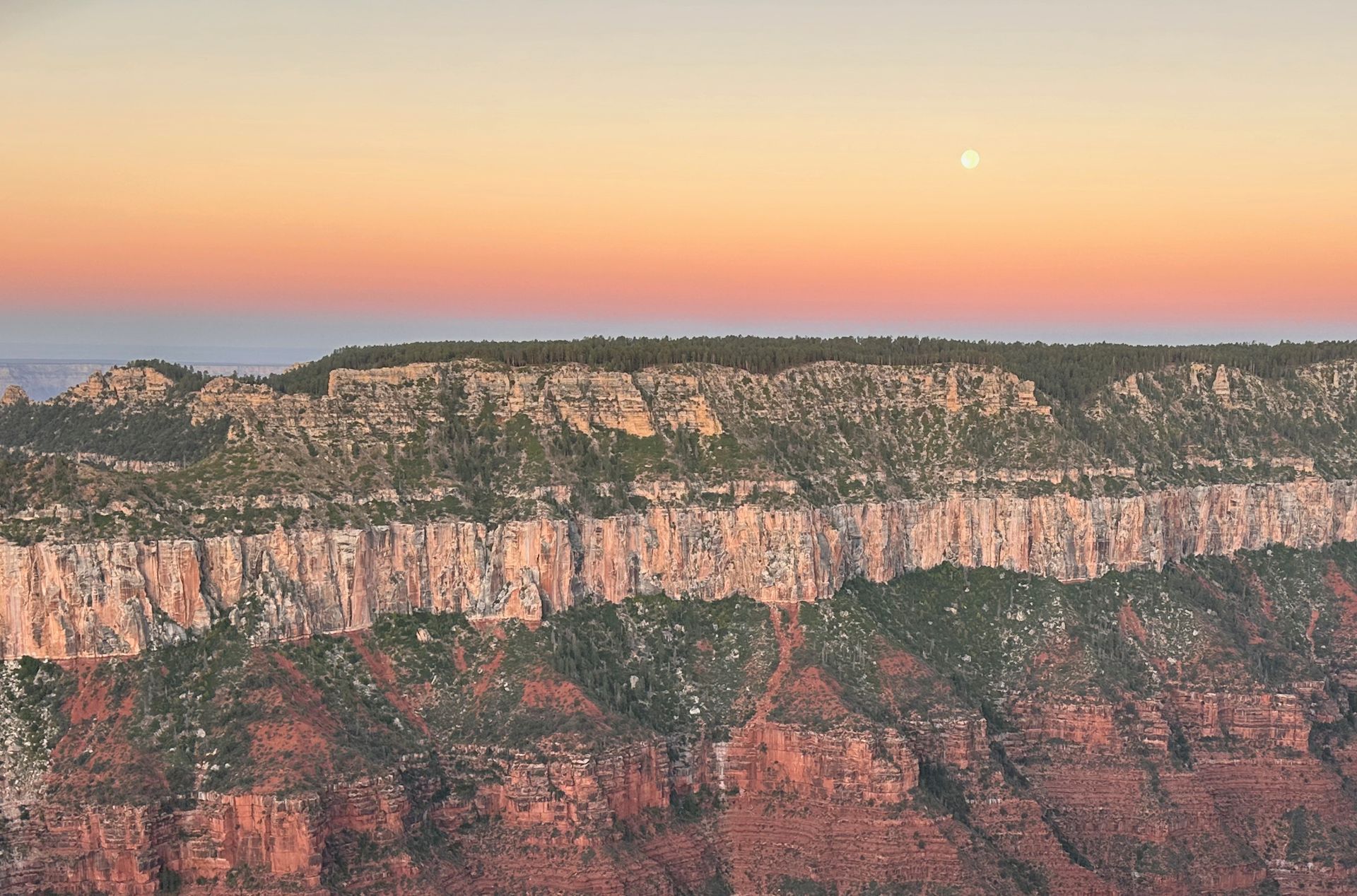 A view of a canyon at sunset with the moon in the sky.