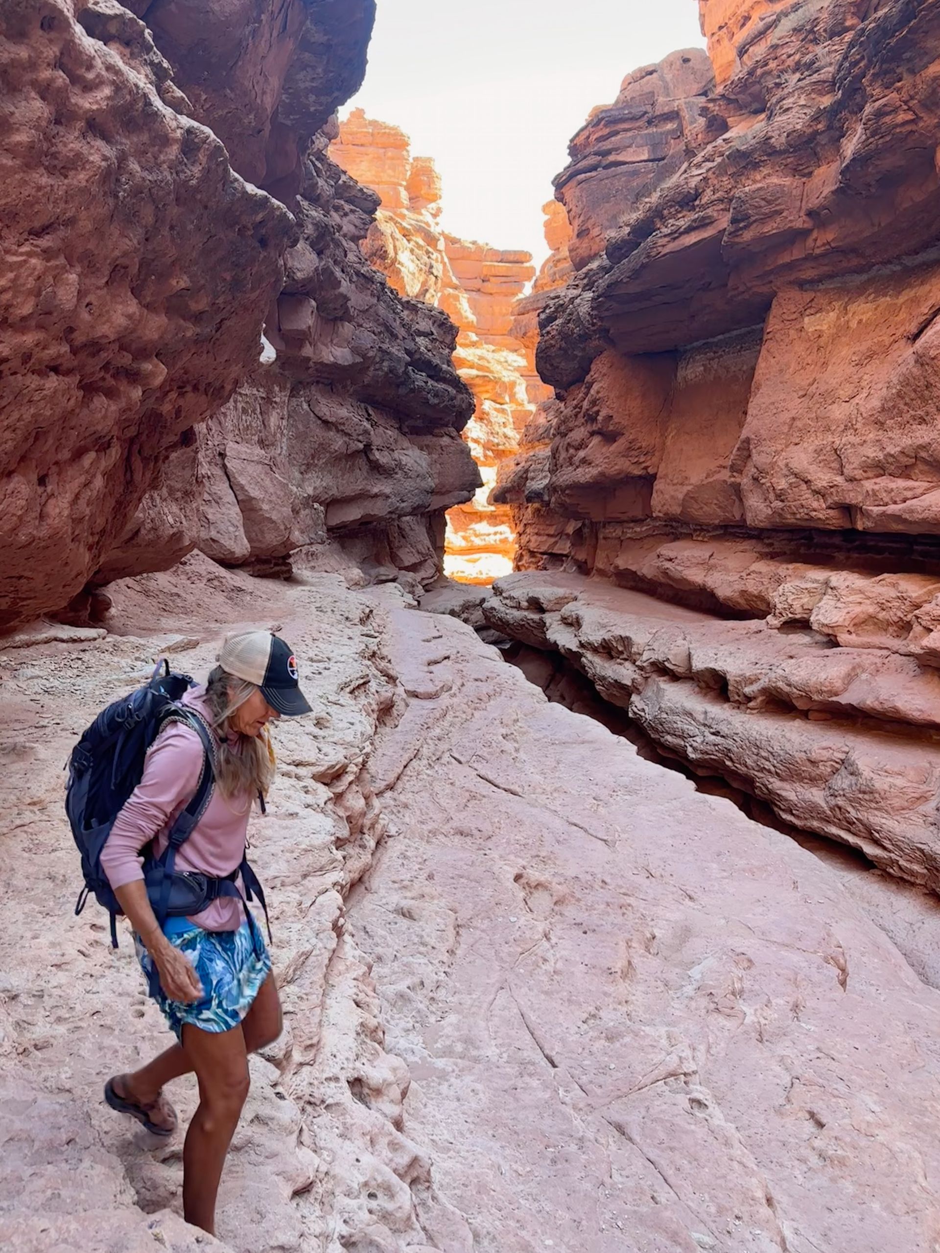 A woman with a backpack is walking through a canyon.