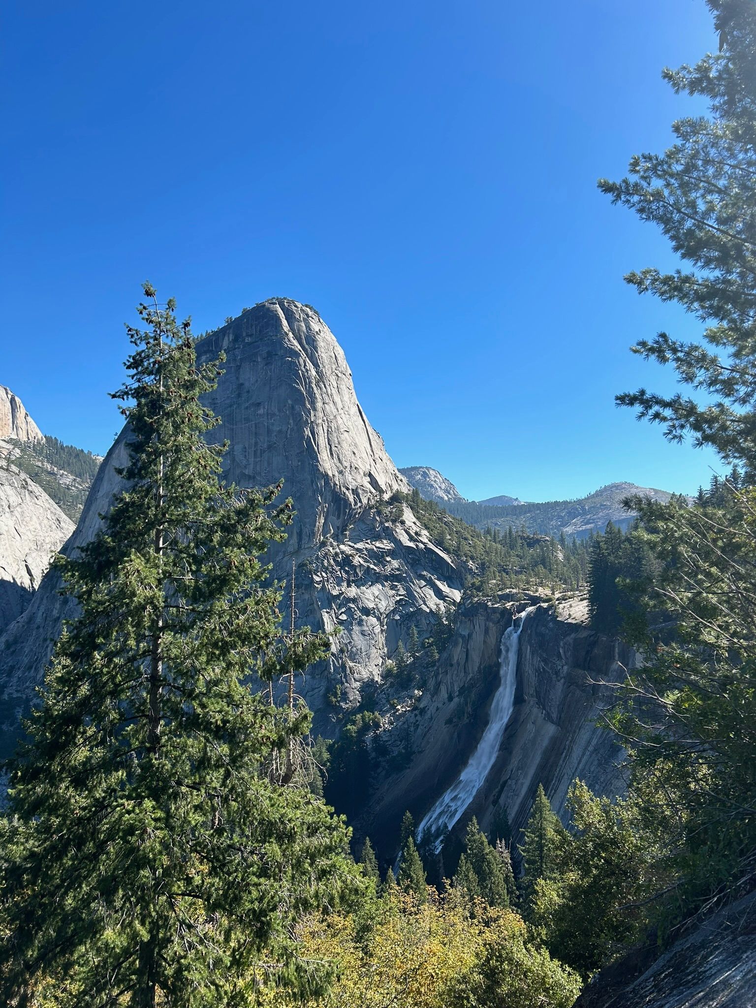 A mountain surrounded by trees and a waterfall on a sunny day.