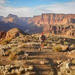 A man is walking through a desert landscape with mountains in the background.