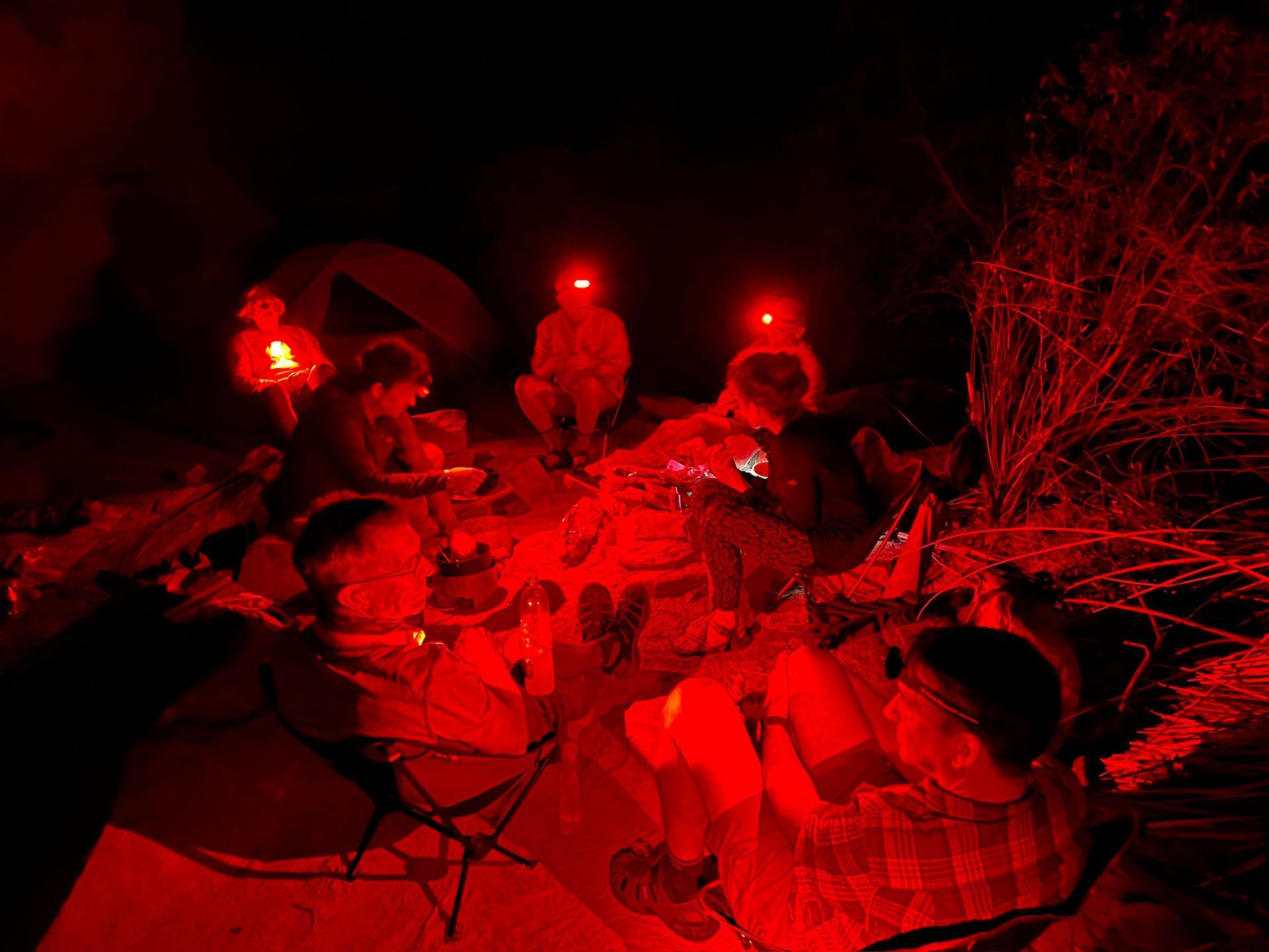 Group of people gathered around a campfire at night, illuminated by red lights.