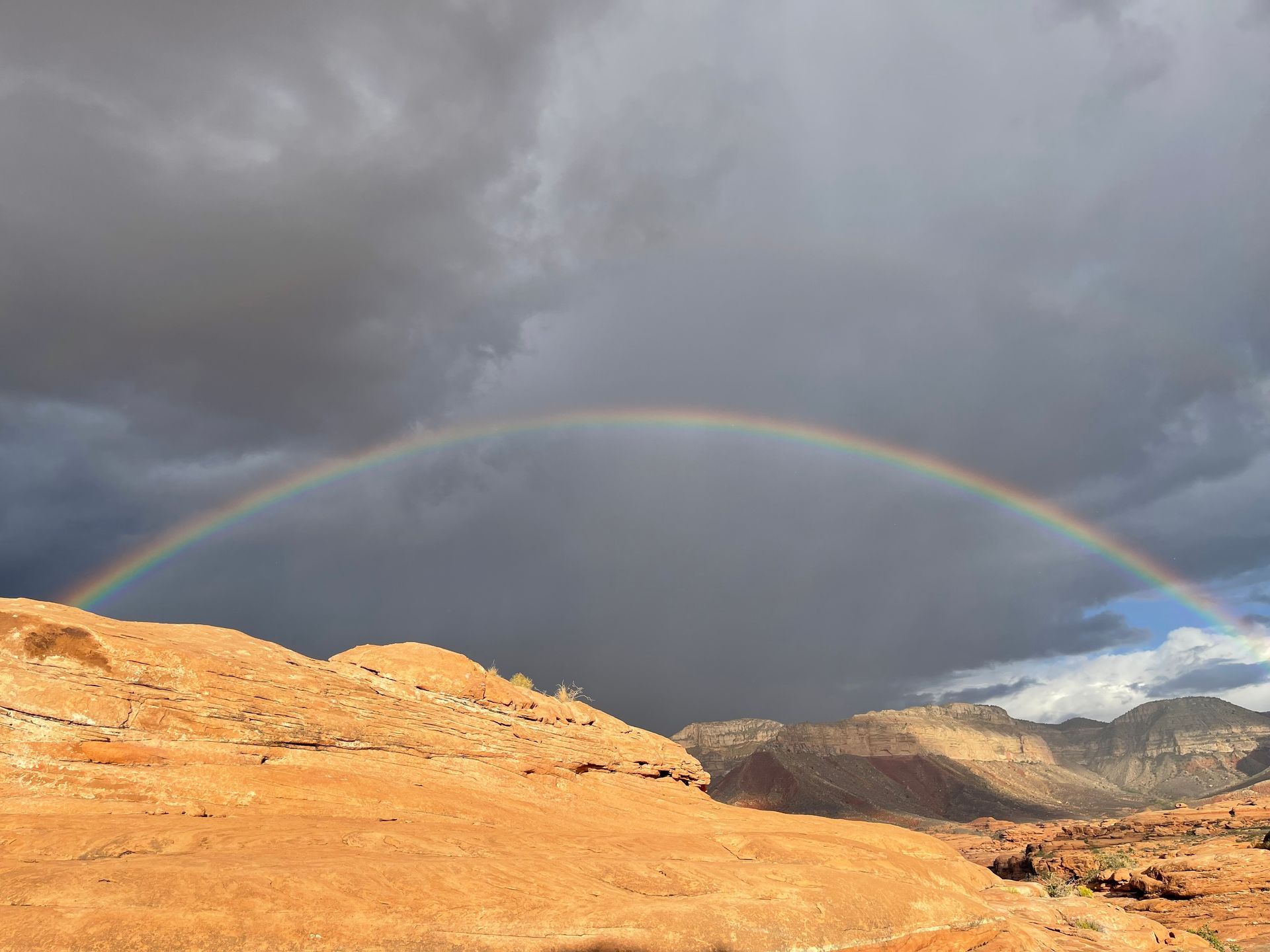 Rainbow arches over red rock desert under a stormy sky.