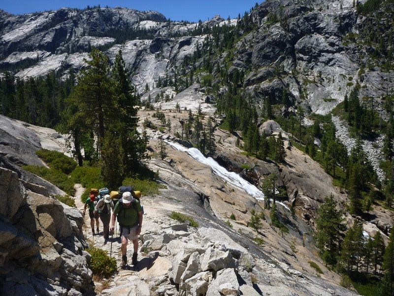 A group of people are hiking up a mountain with a waterfall in the background