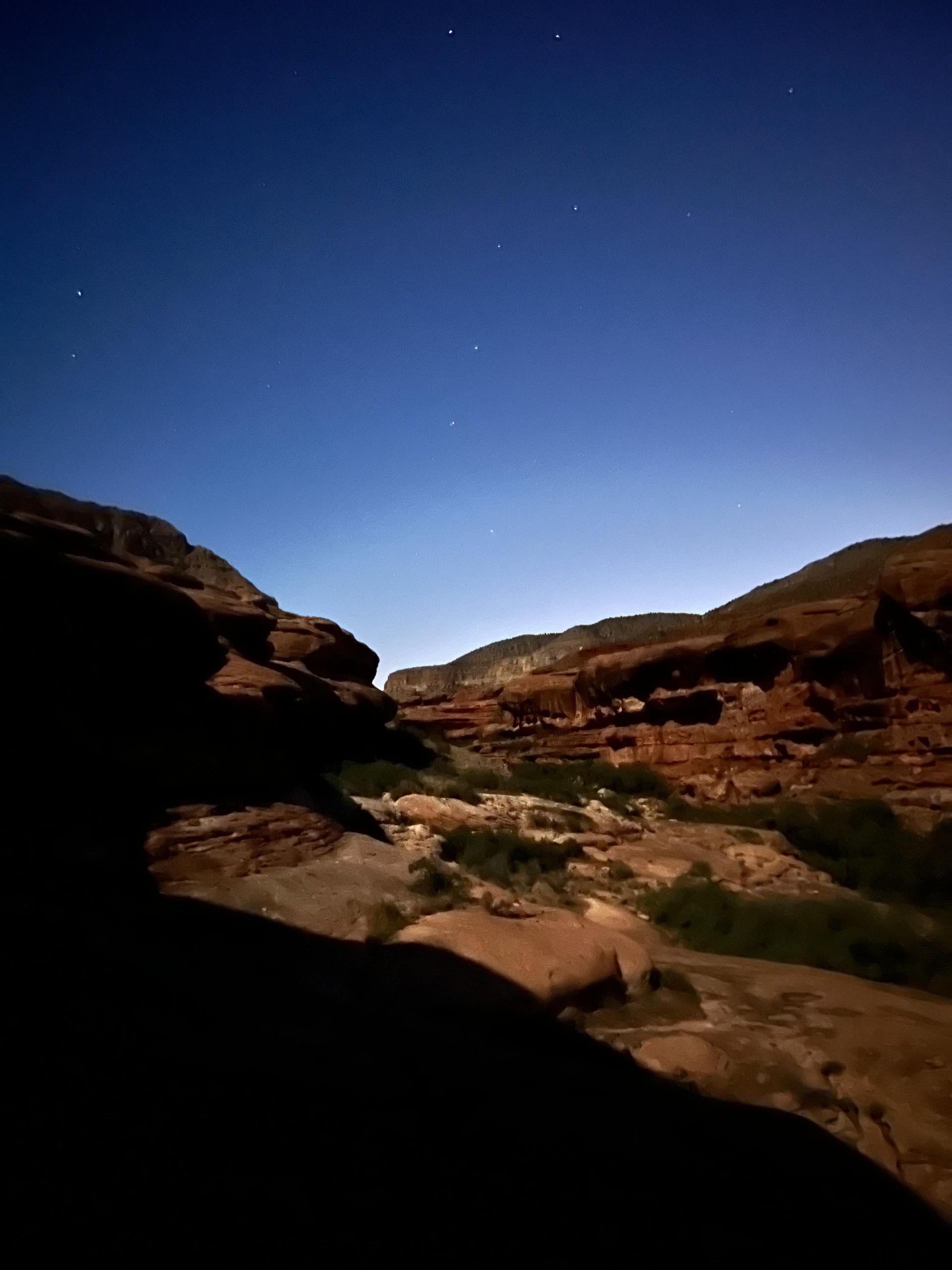 Night landscape of a canyon with dark rock formations under a starry blue sky.
