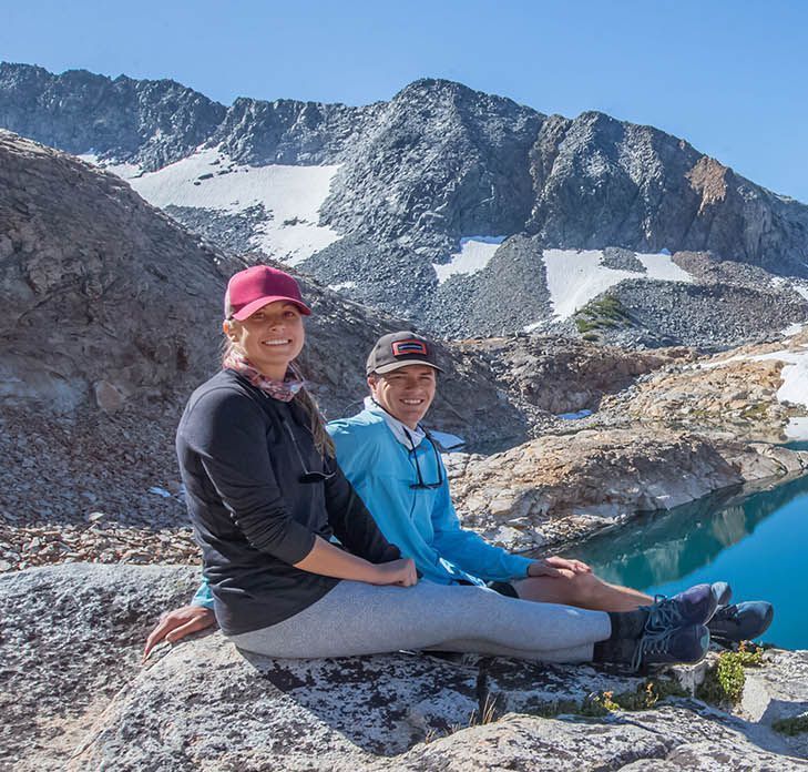 A Man and a Woman Are Sitting on a Rock With Mountains in the Background