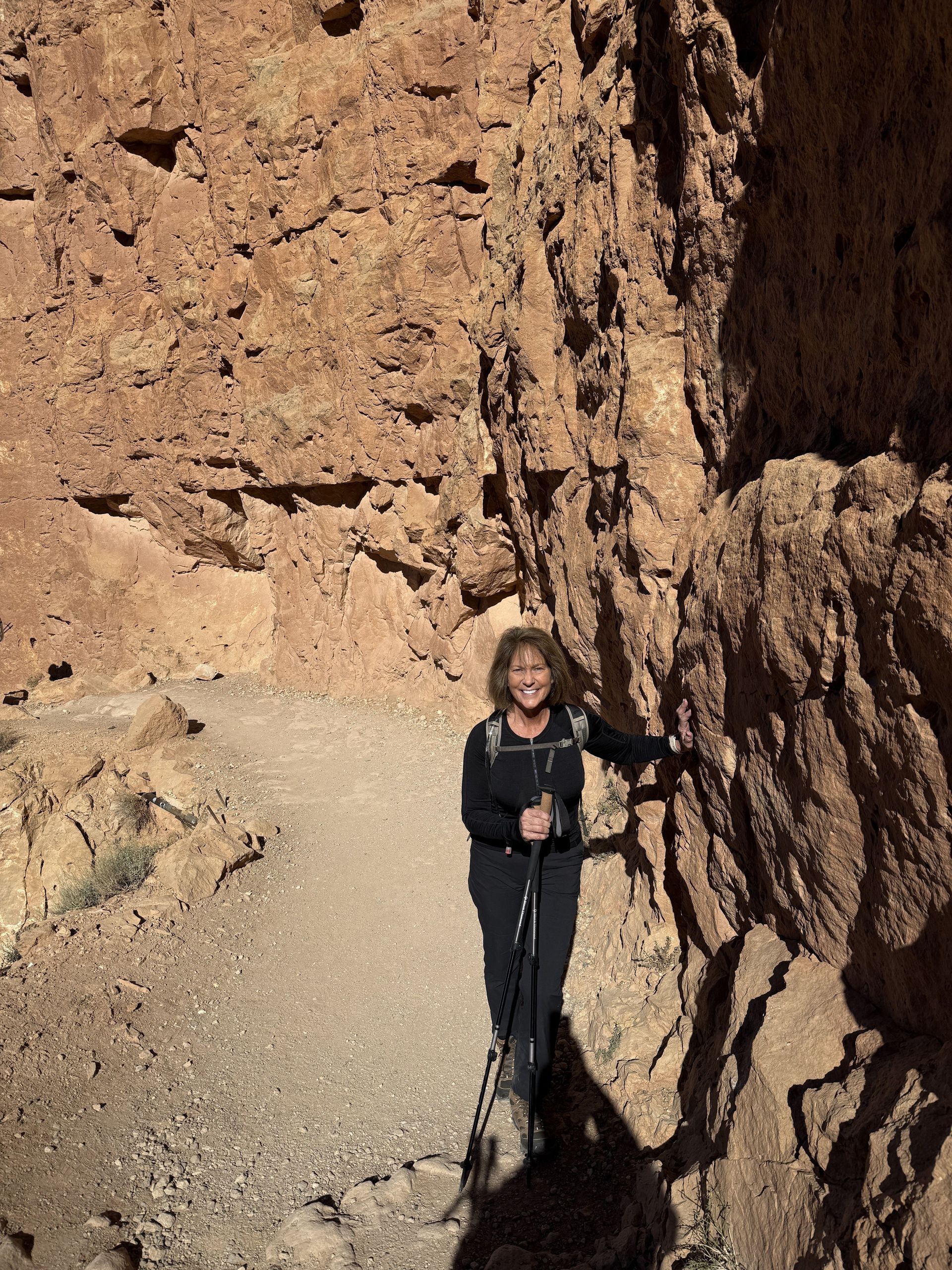 Woman hikes along a narrow path beside a red-rock canyon wall, using trekking poles.