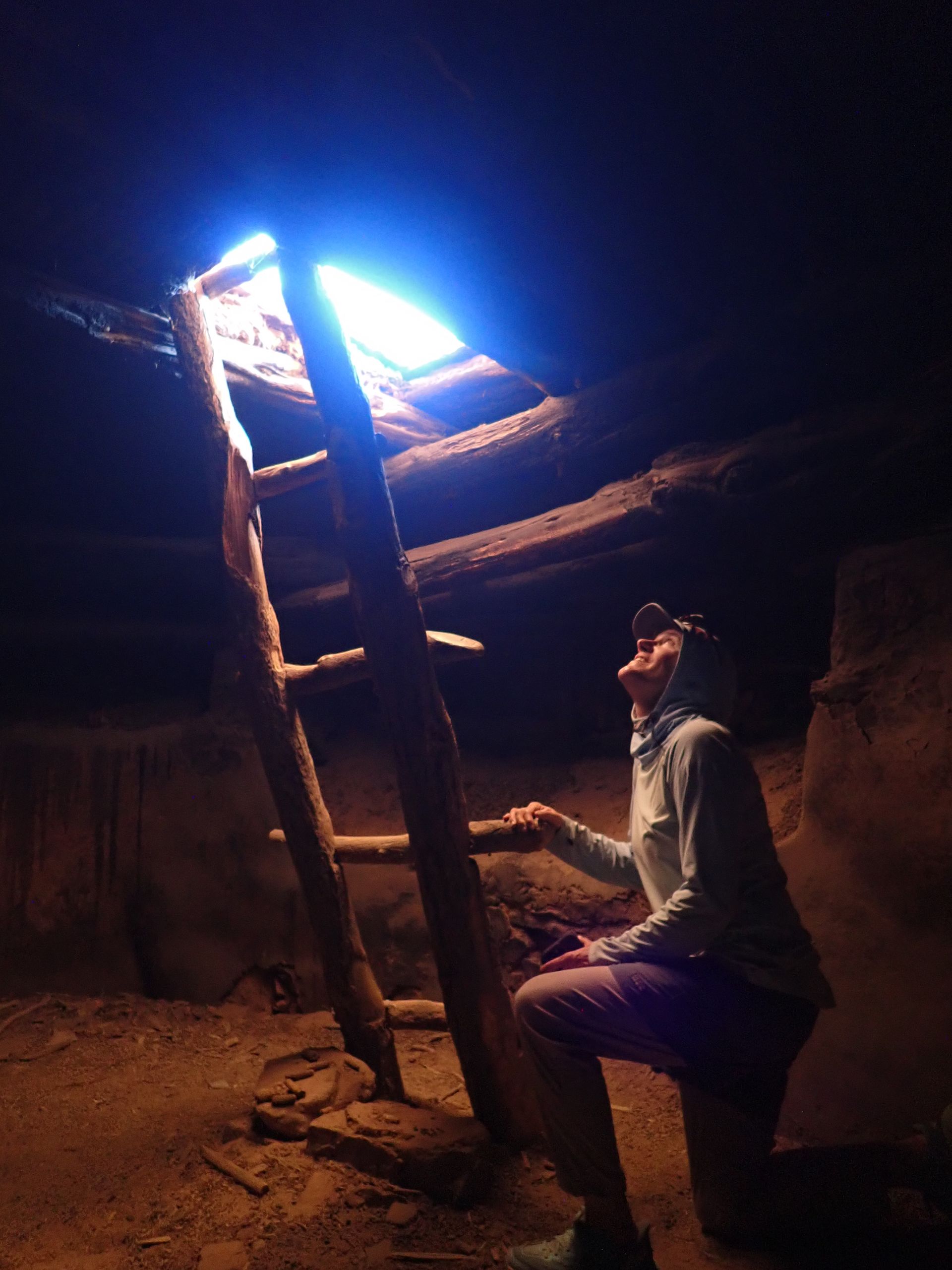 A person is kneeling down in a dark room looking up at a ladder.