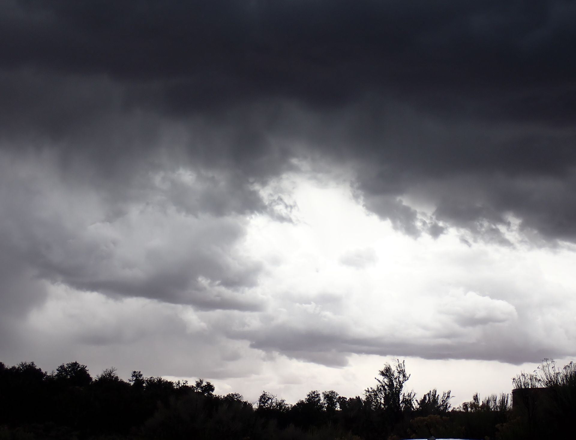 A dark cloudy sky with trees in the foreground