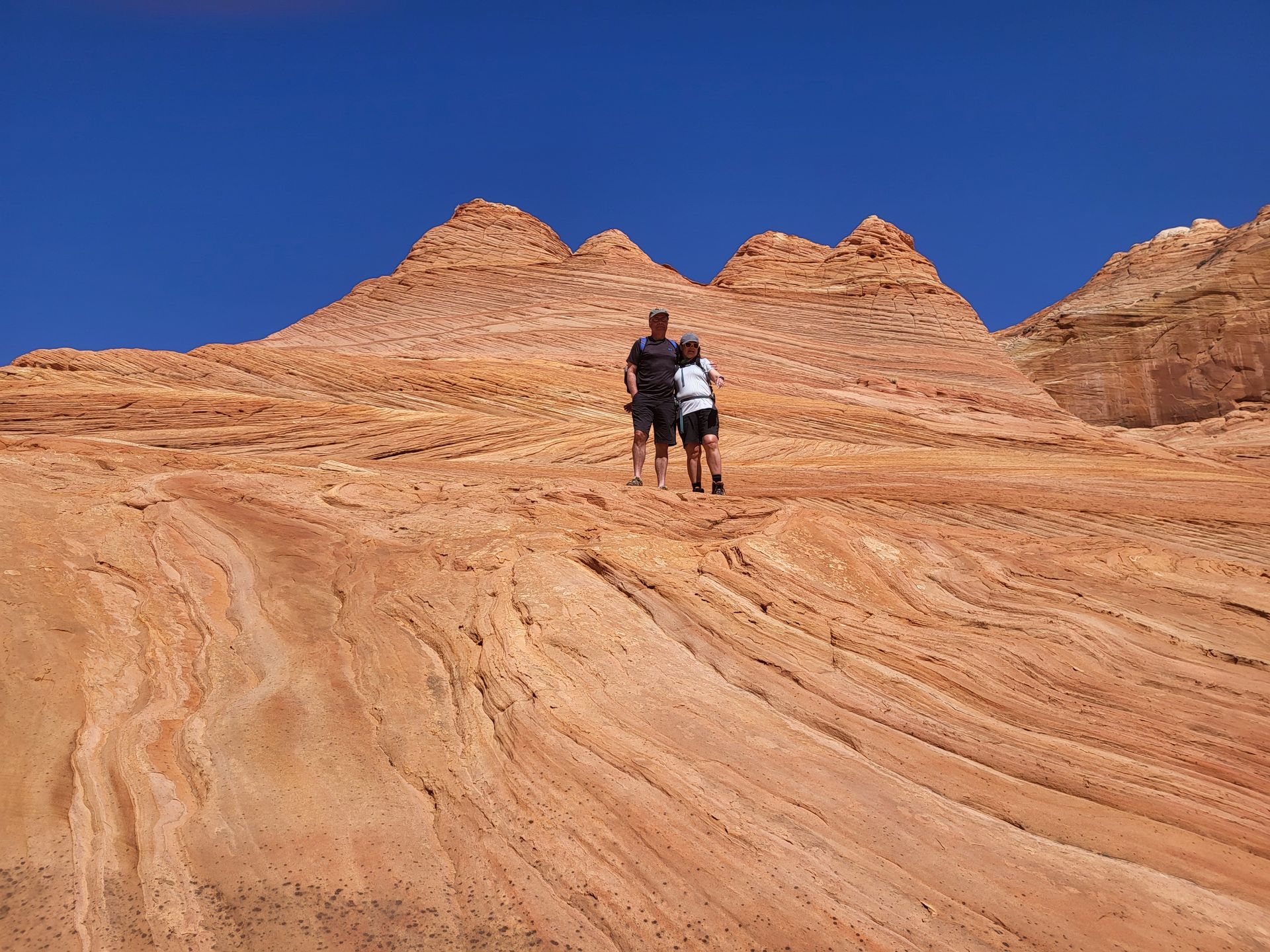 Two people hiking on reddish-orange sandstone under a clear blue sky.