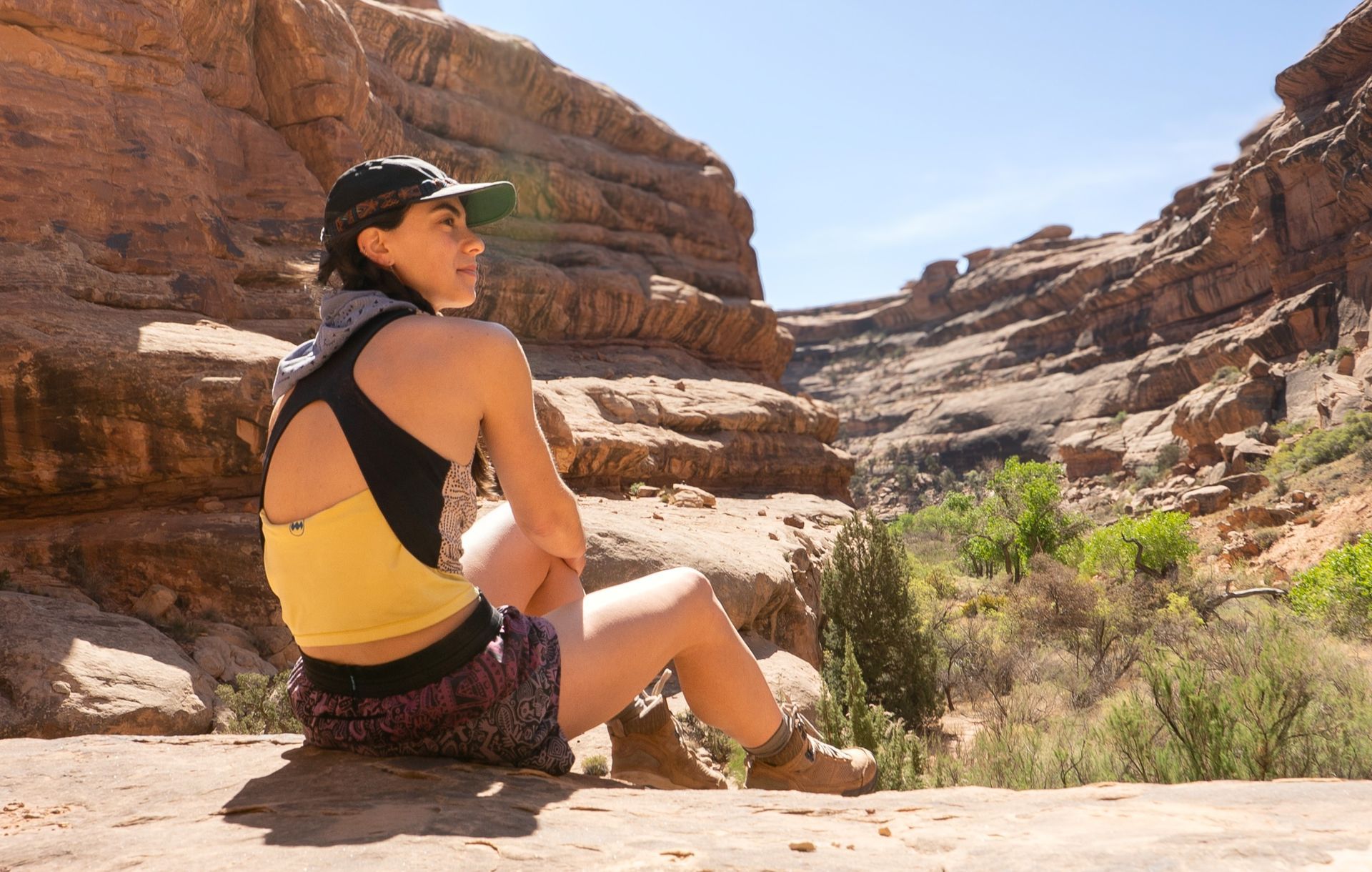 A woman is sitting on a rock looking out over a canyon.