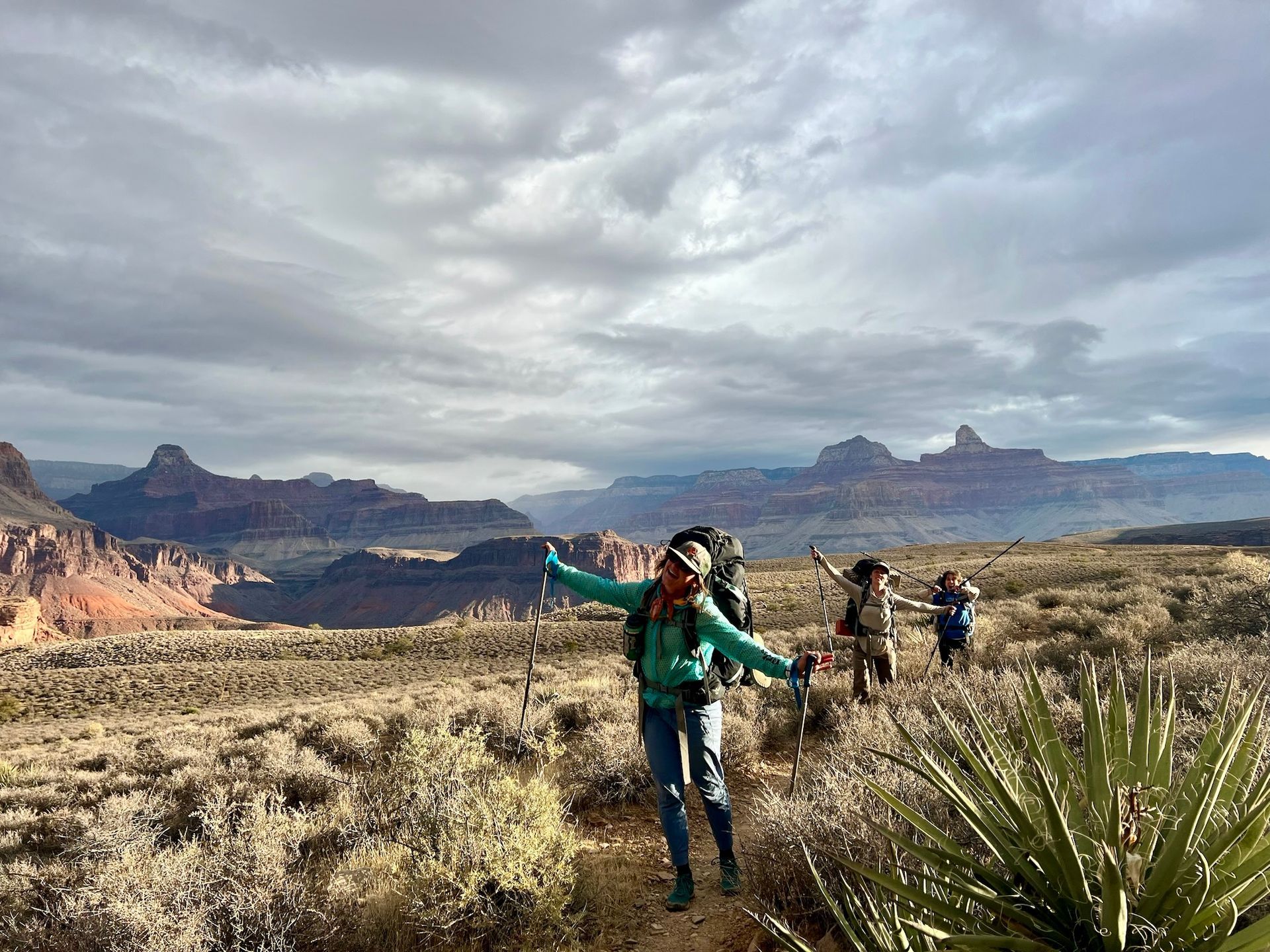 A group of people are hiking in the desert with mountains in the background.