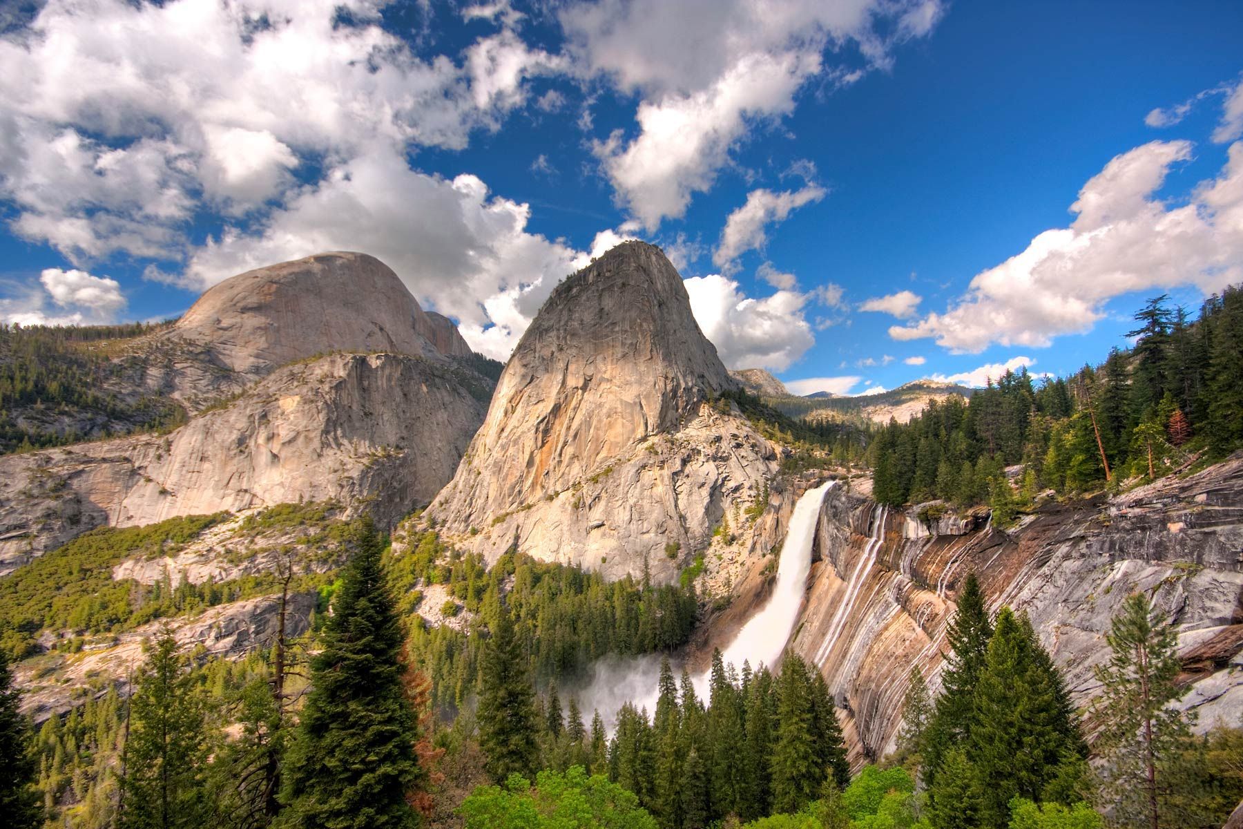 Waterfall in the middle of the mountains surrounded by trees.