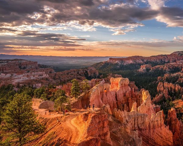 Sunset over red rock hoodoos and pine-covered canyon under a dramatic cloudy sky