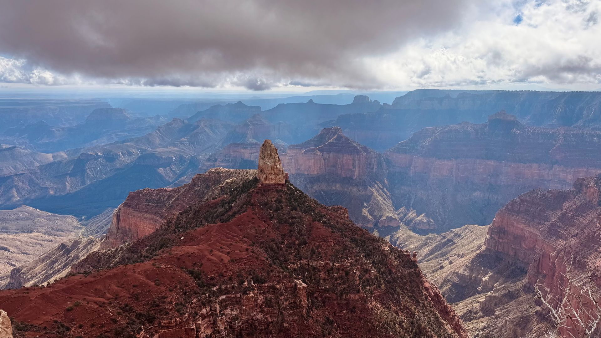 Grand Canyon vista with a prominent rock spire, under a cloudy sky.