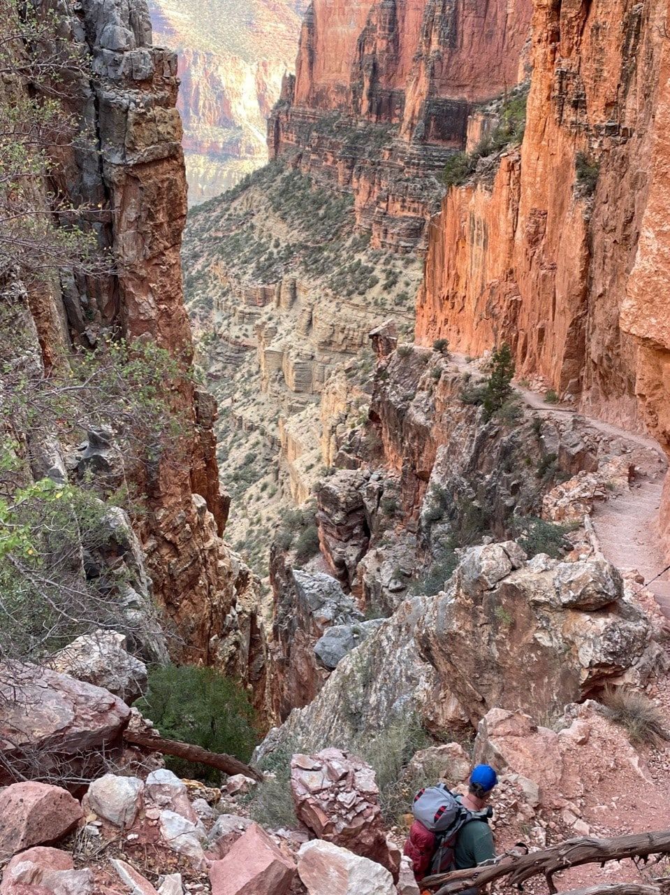 A person with a backpack is walking down a trail in a canyon.