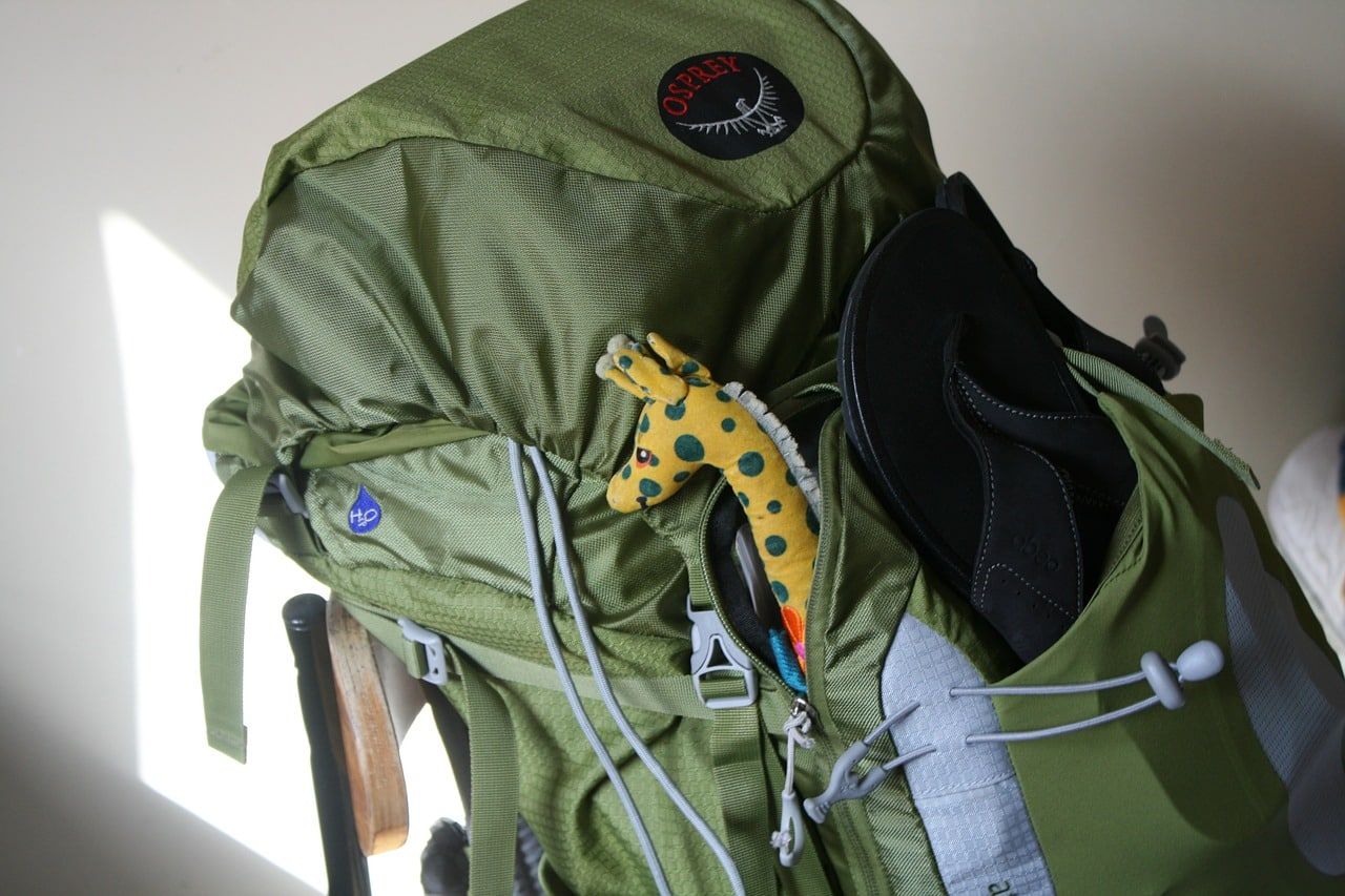 A green osprey backpack with a stuffed giraffe in the front pocket