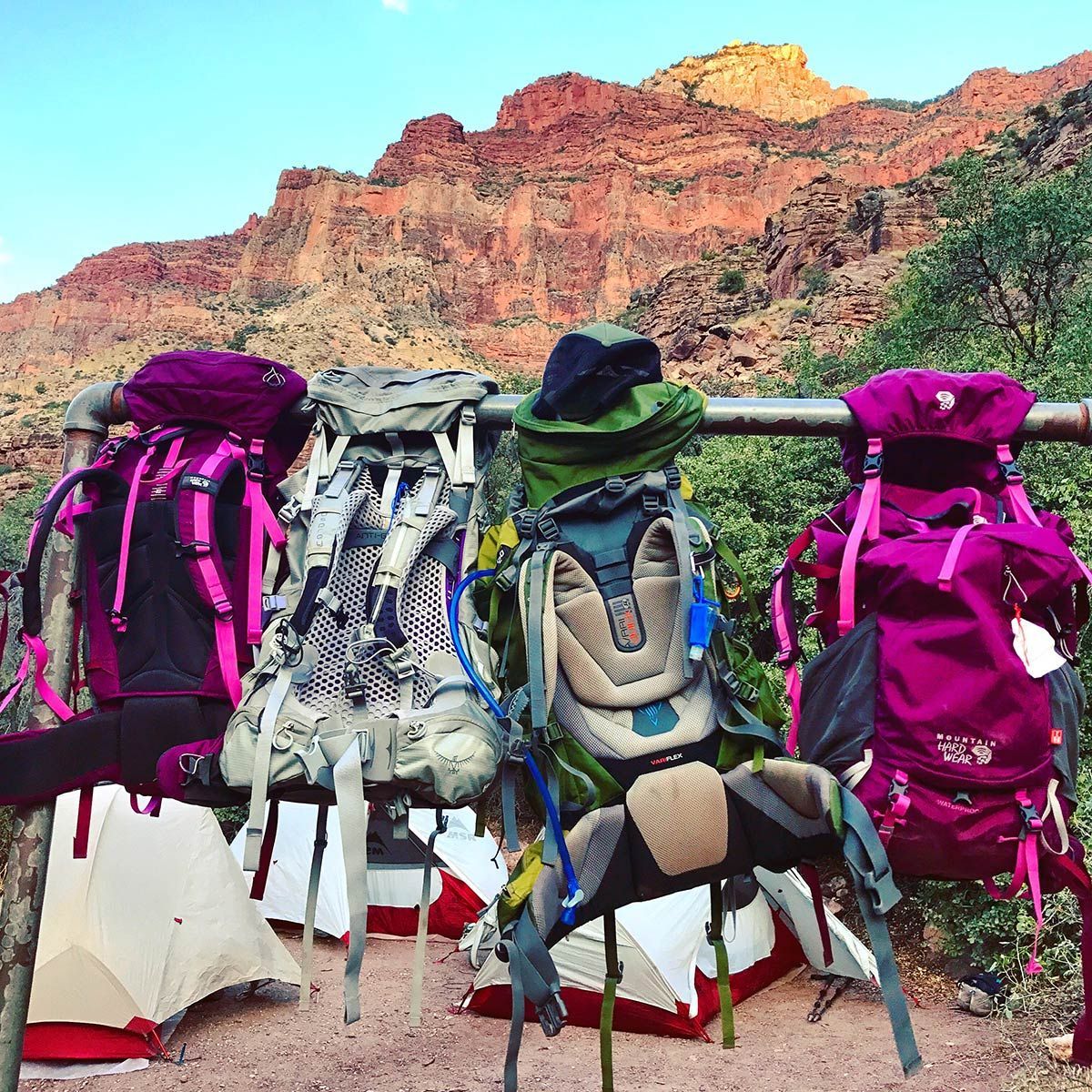 A bunch of backpacks are stacked on top of each other on a bench.