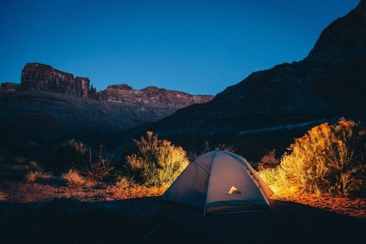 A tent is lit up in the mountains at night.