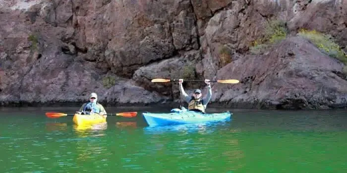 Two people are rowing kayaks on a lake.