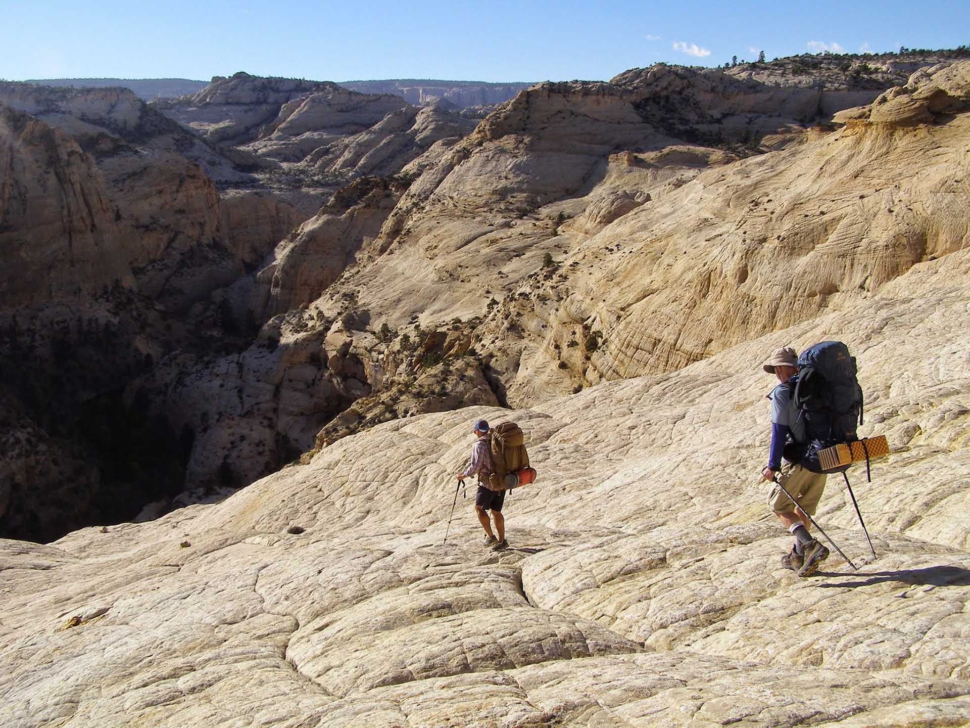 Two people with backpacks are walking down a rocky hillside.