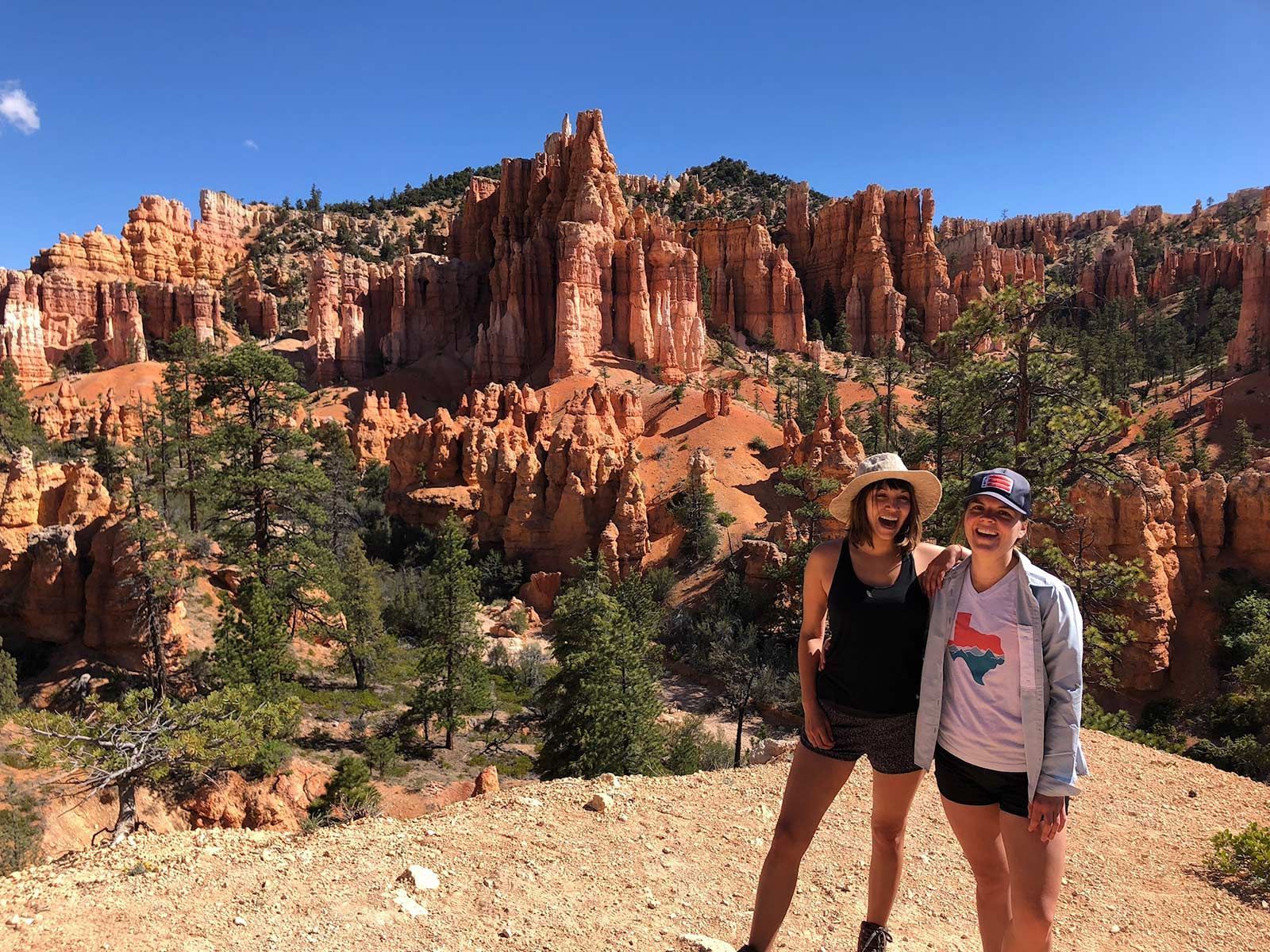 Two women are standing next to each other in front of a mountain.