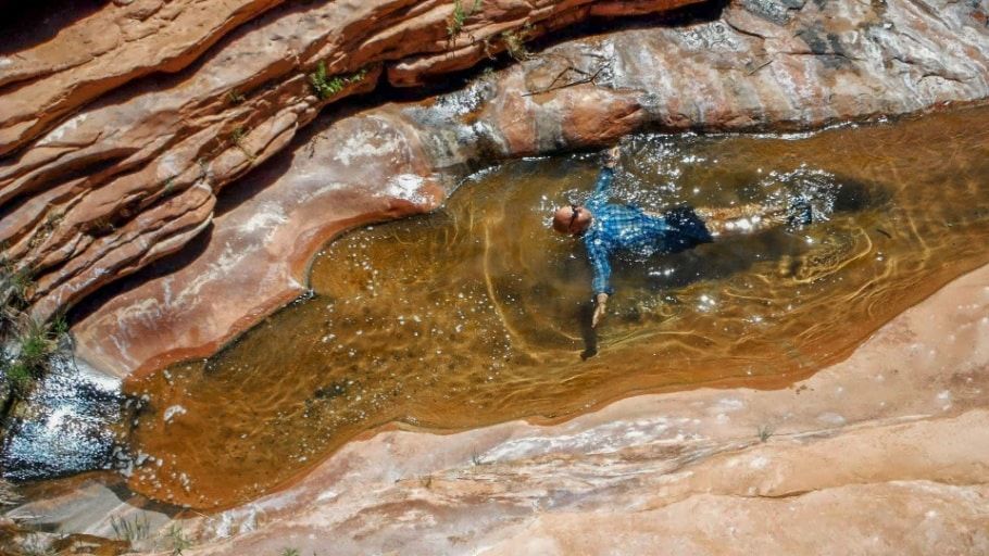 A person is laying in a pool of water surrounded by rocks.