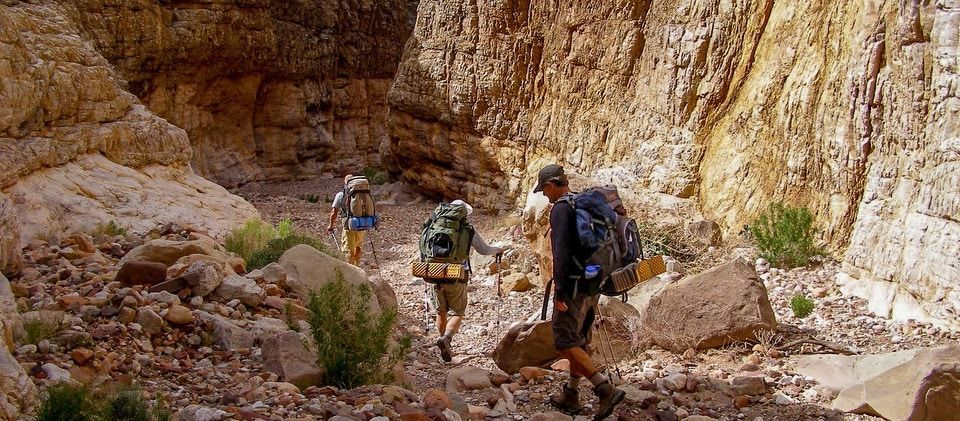 Two people with backpacks are walking through a rocky canyon.