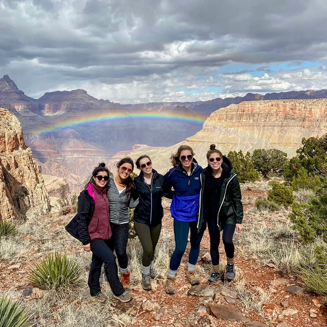 A group of women are posing for a picture with a rainbow in the background.