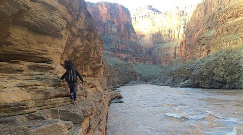 A person is walking along a cliff overlooking a river.