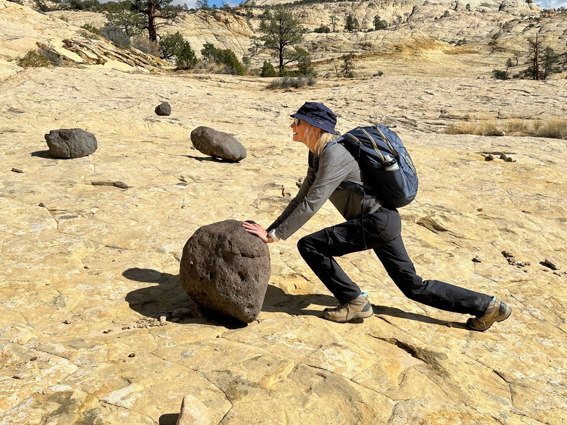 A man is pushing a large rock in the desert.